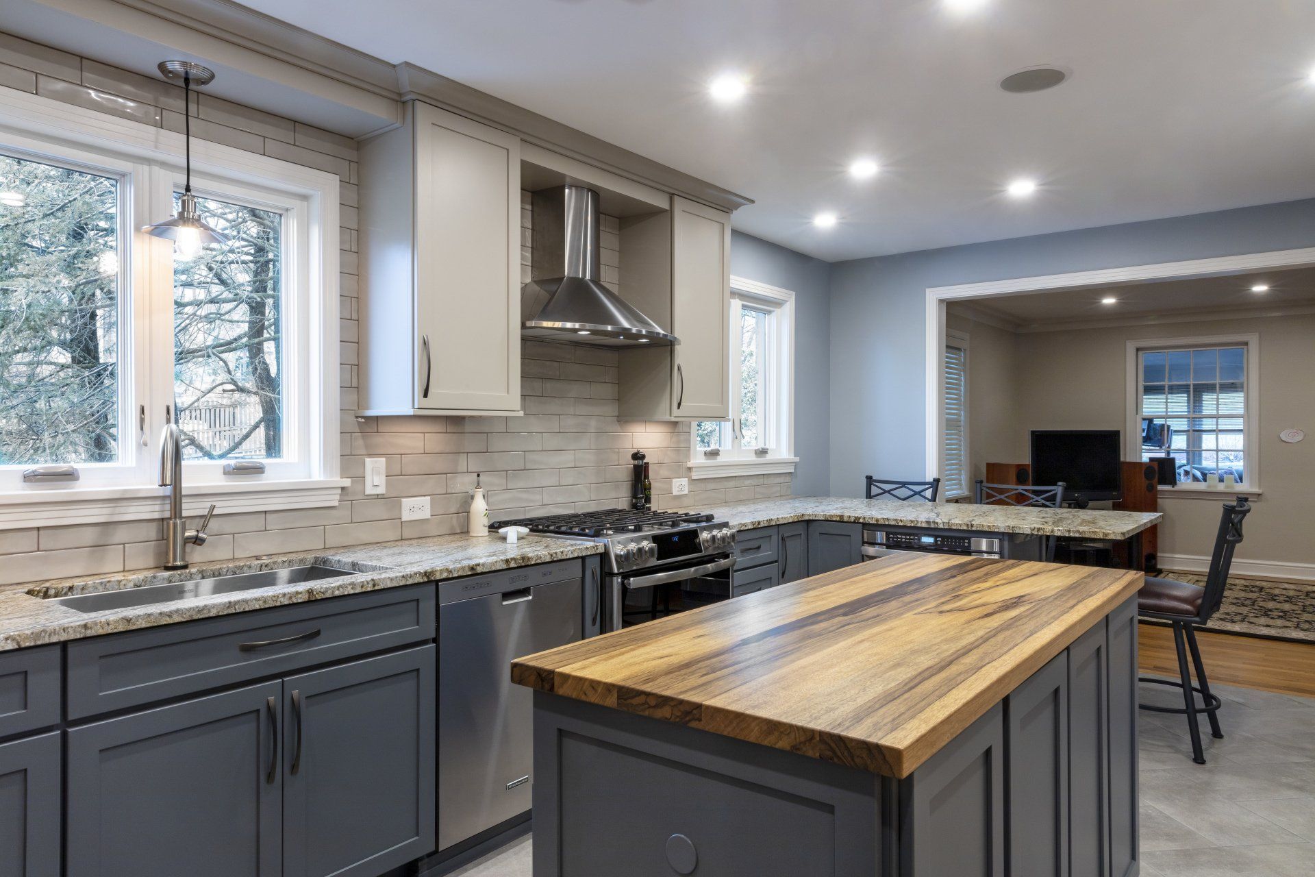 Modern kitchen with gray cabinets, island, granite counters, stainless range, and bright windows