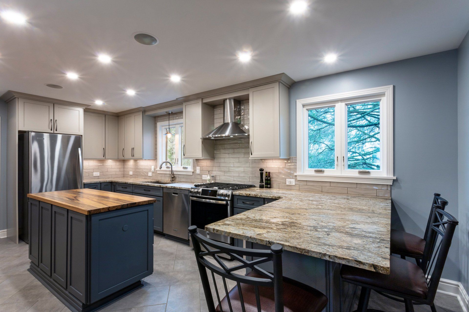 Modern kitchen with gray cabinets, granite island, stainless steel appliances, and a small dining table by the window.
