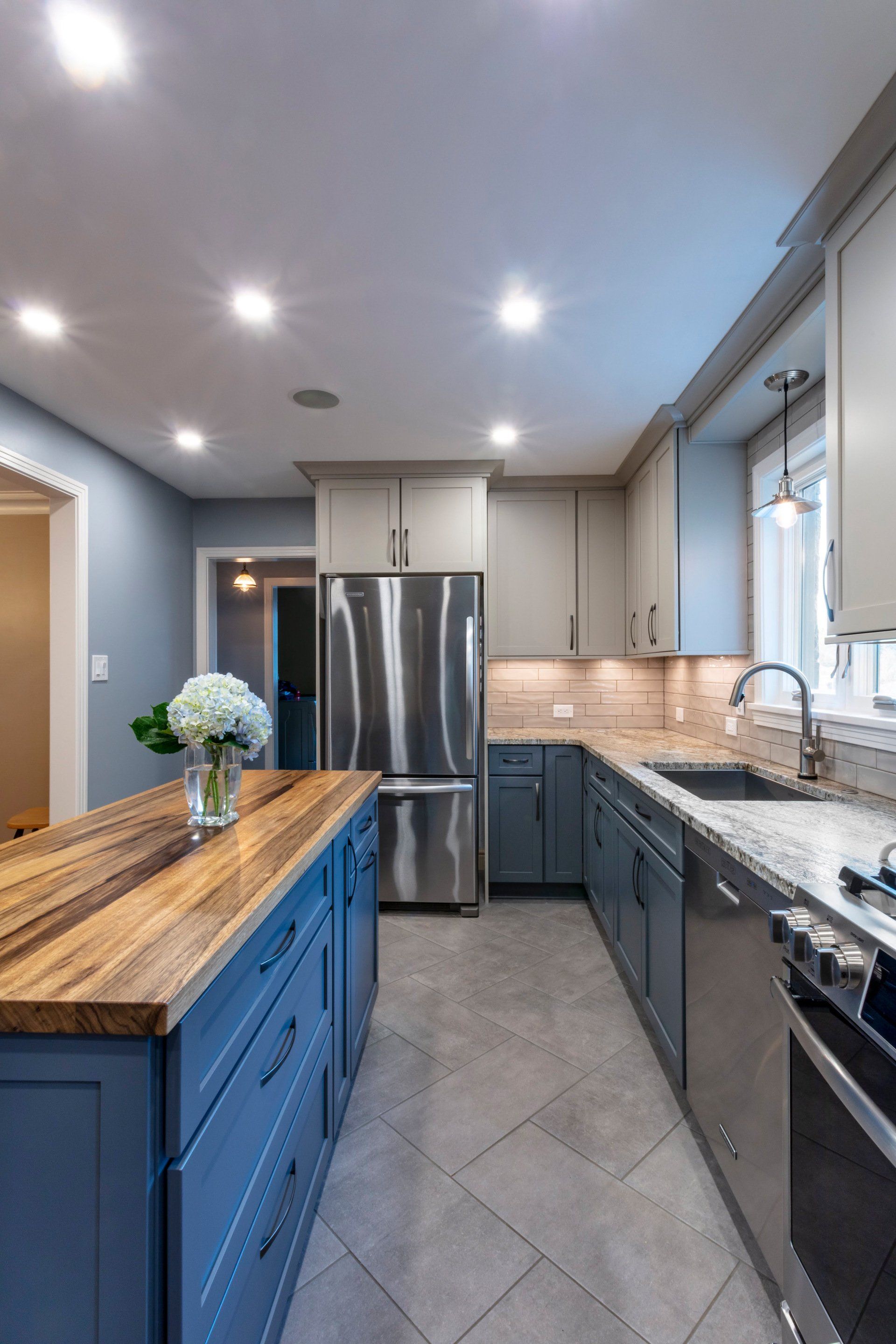Modern kitchen with blue island, stainless steel fridge, gray cabinets, and wood countertop