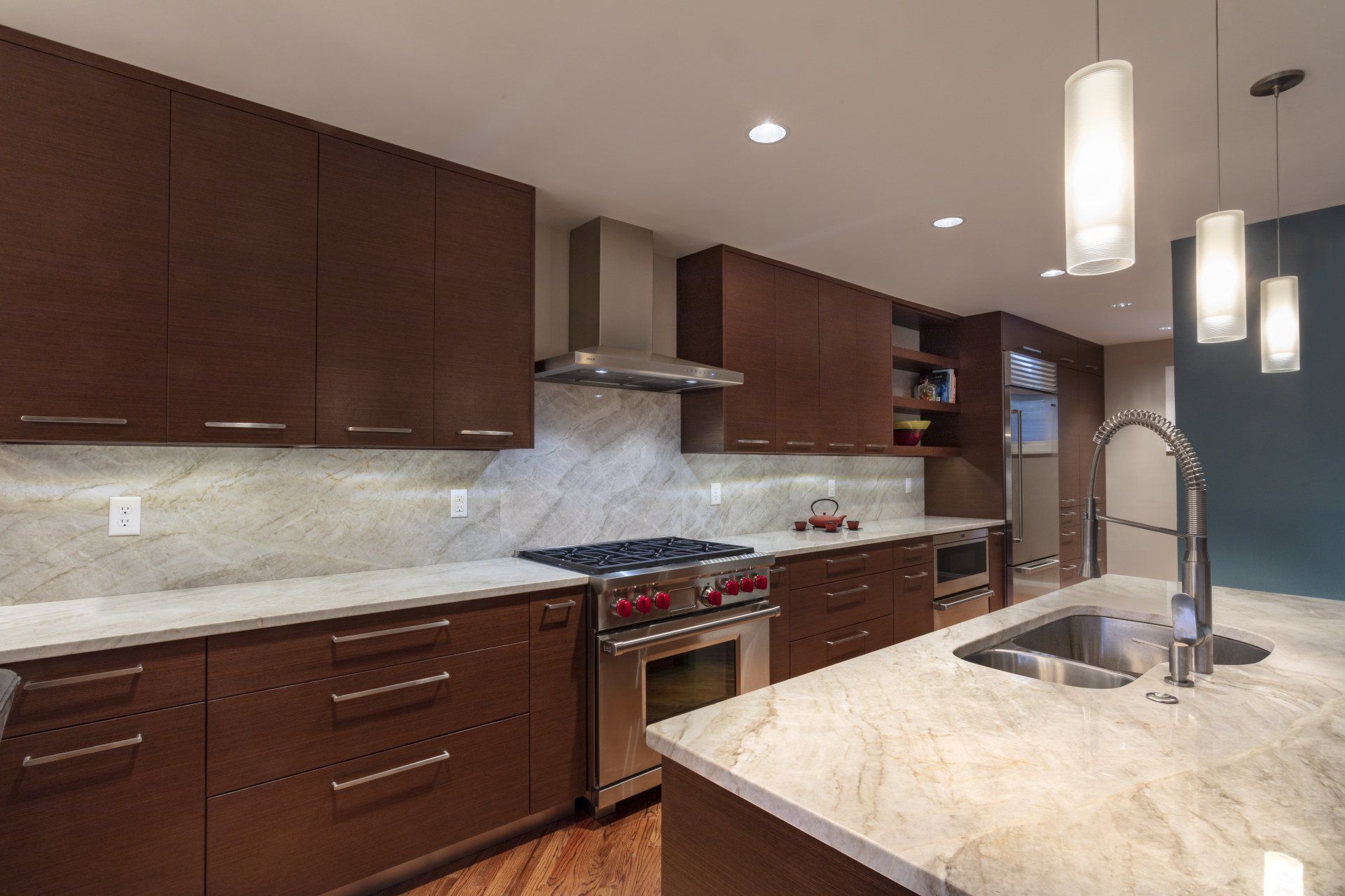 Modern kitchen with dark wood cabinets, marble counters, stainless appliances, and pendant lights