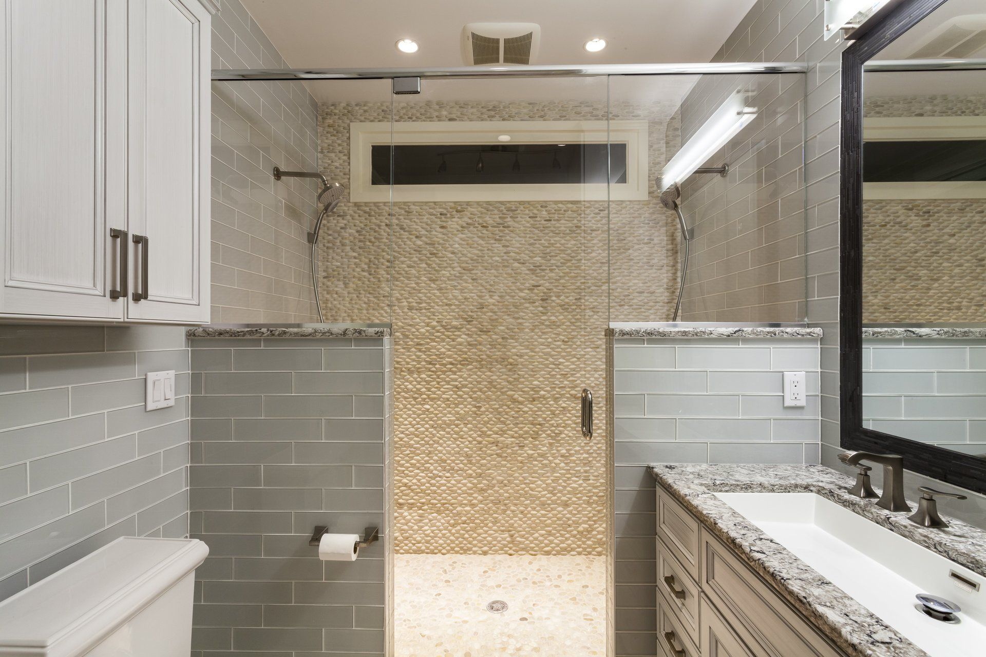 Modern bathroom with glass shower, gray tile, and marble vanity under bright lights