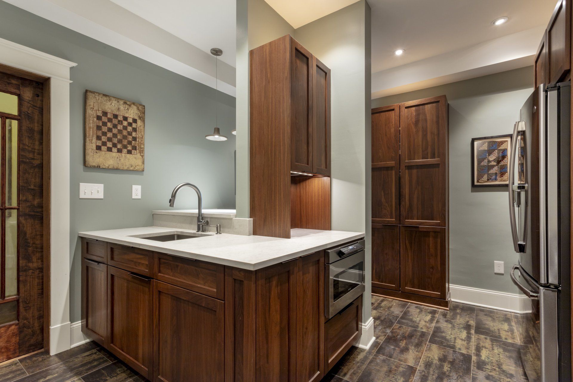 Modern kitchen with dark wood cabinets, white countertops, and stainless steel refrigerator in a narrow layout