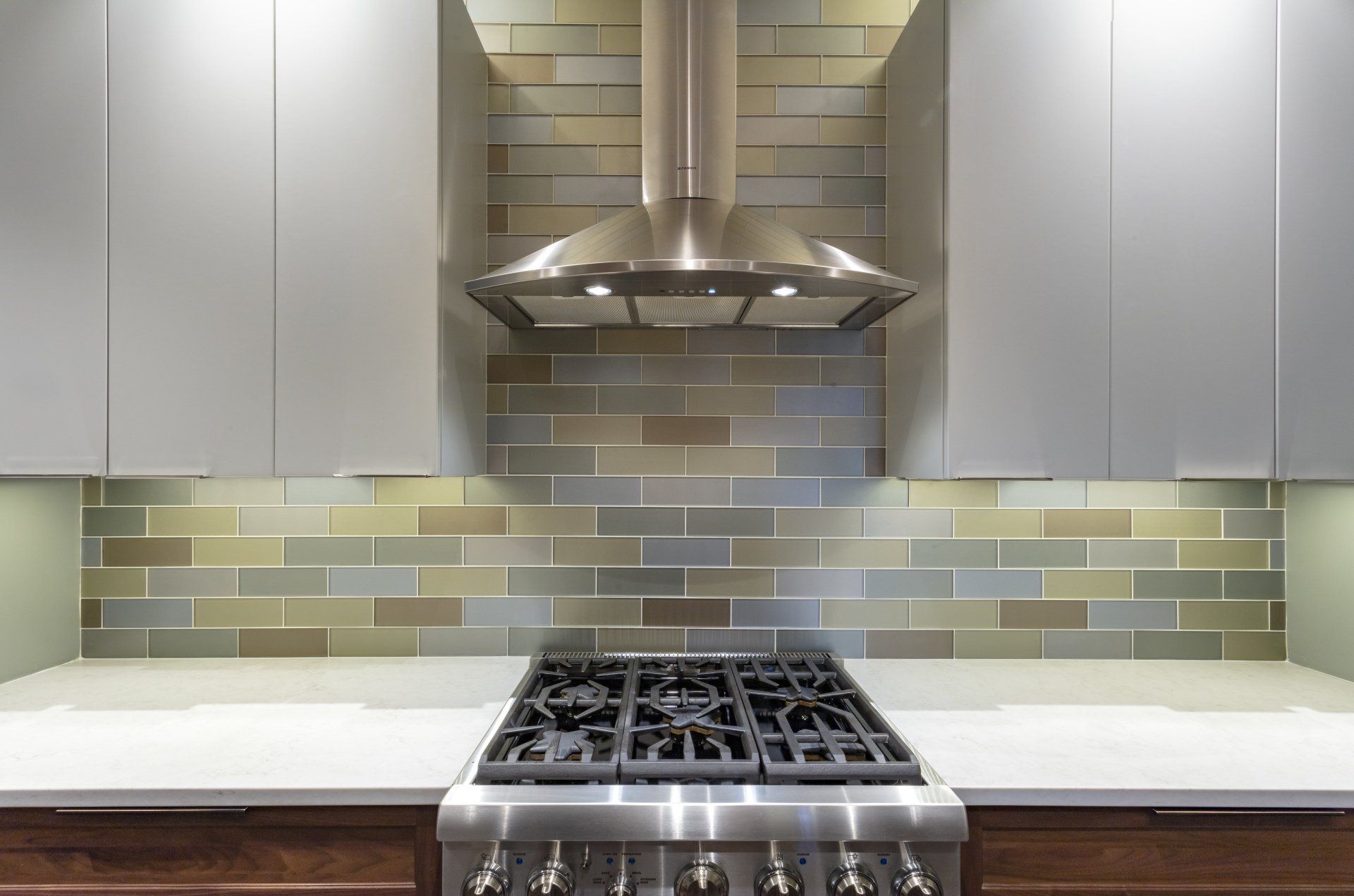 Modern kitchen with stainless steel stove, range hood, and gray tile backsplash