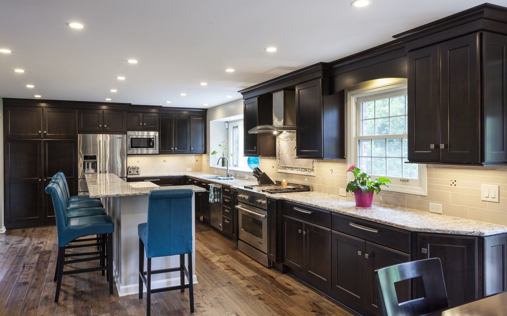 Modern kitchen with dark cabinets, stainless appliances, granite counters, and two blue bar stools.