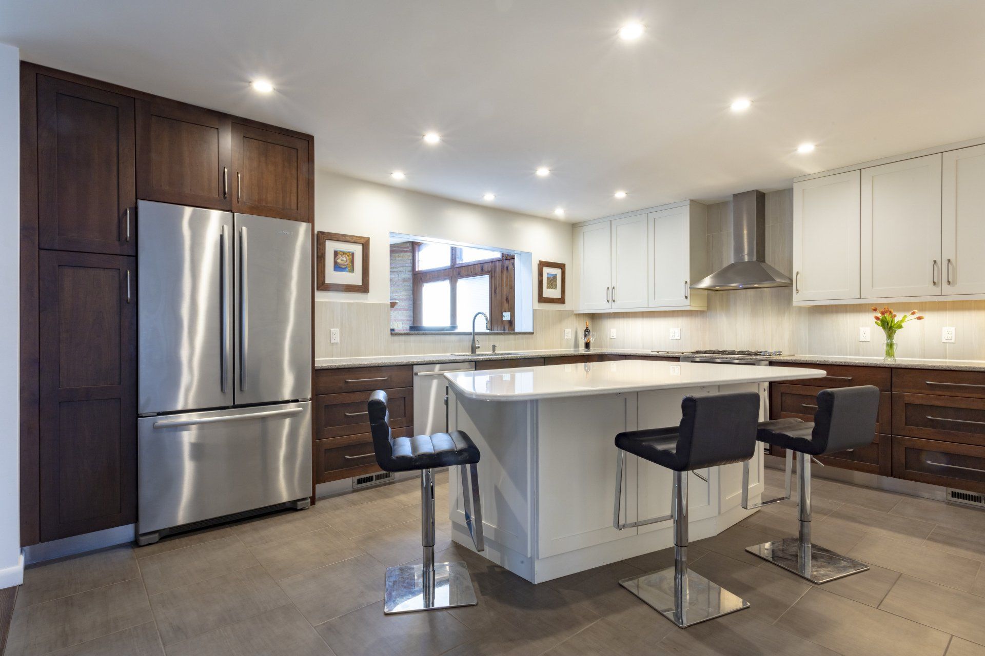 Modern kitchen with stainless steel appliances, white island, and two black stools under recessed lights