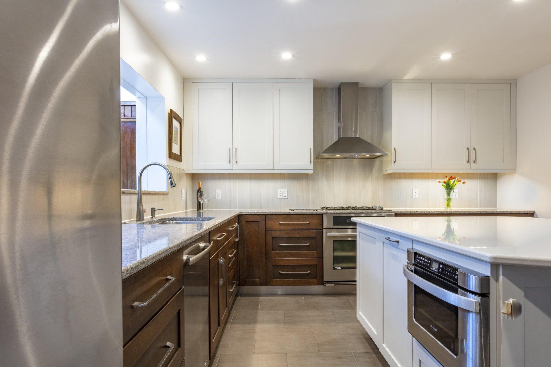 Bright modern kitchen with white cabinets, dark wood drawers, stainless appliances, and a central island.