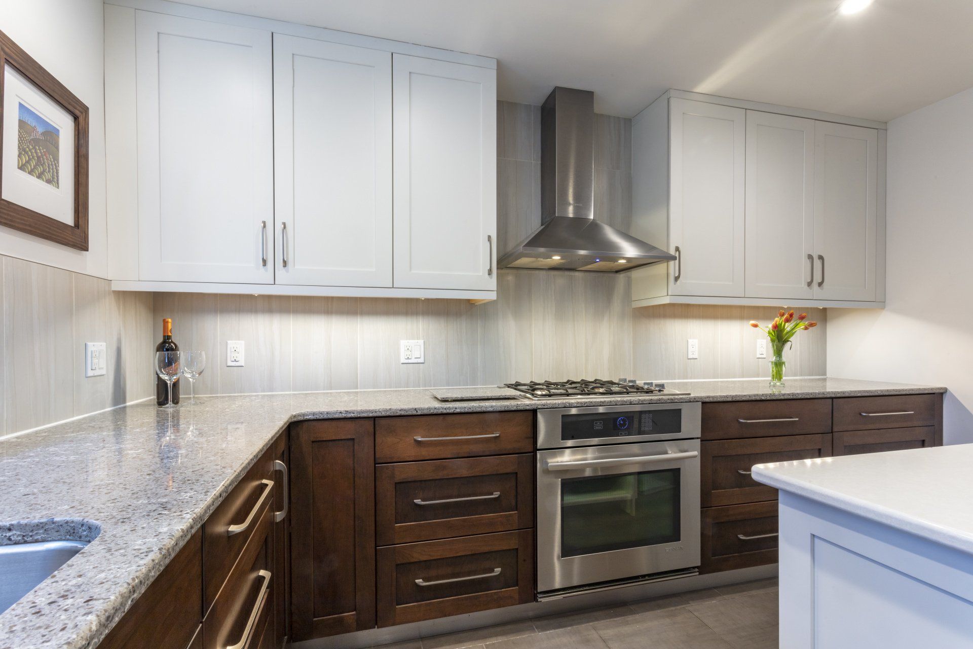 Modern kitchen with white cabinets, dark wood lower cabinets, stainless-steel oven, and gray countertops