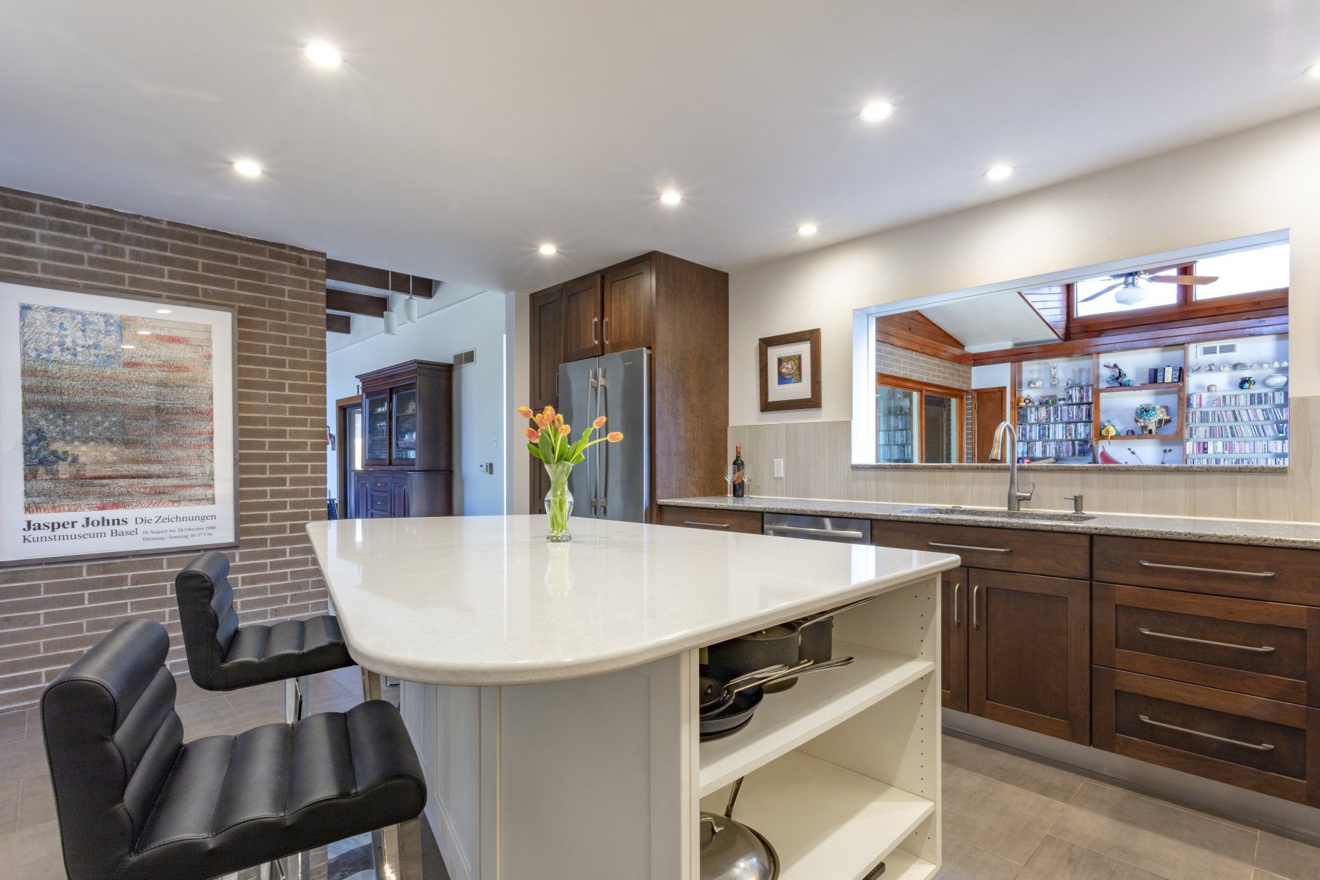 Modern kitchen with white island, black stools, wood cabinets, and a large pass-through window