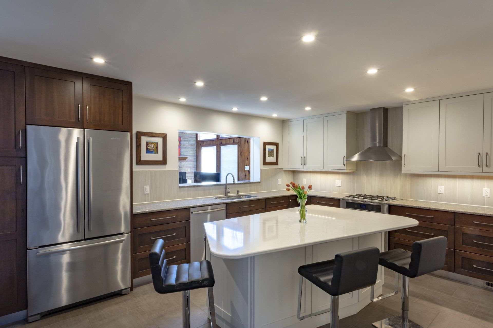 Modern kitchen with stainless steel appliances, white island, dark barstools, and recessed lighting.