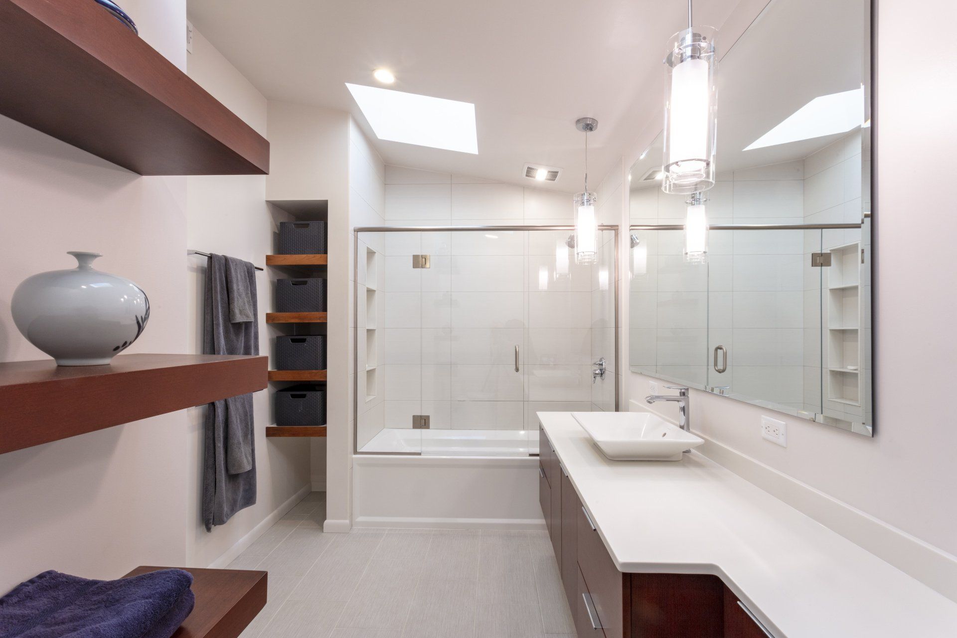 Modern bathroom with double vanity, large mirrors, glass shower, and skylight