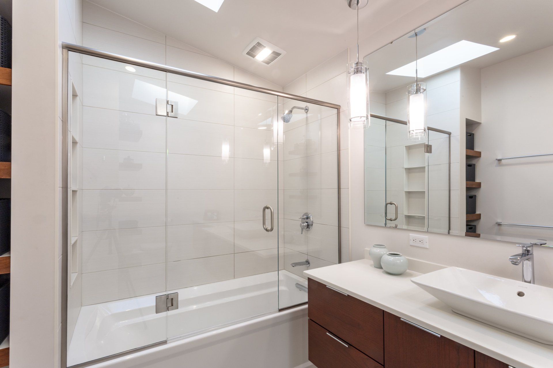 Bright modern bathroom with a glass-enclosed tub, vanity, mirror, and white tile walls.