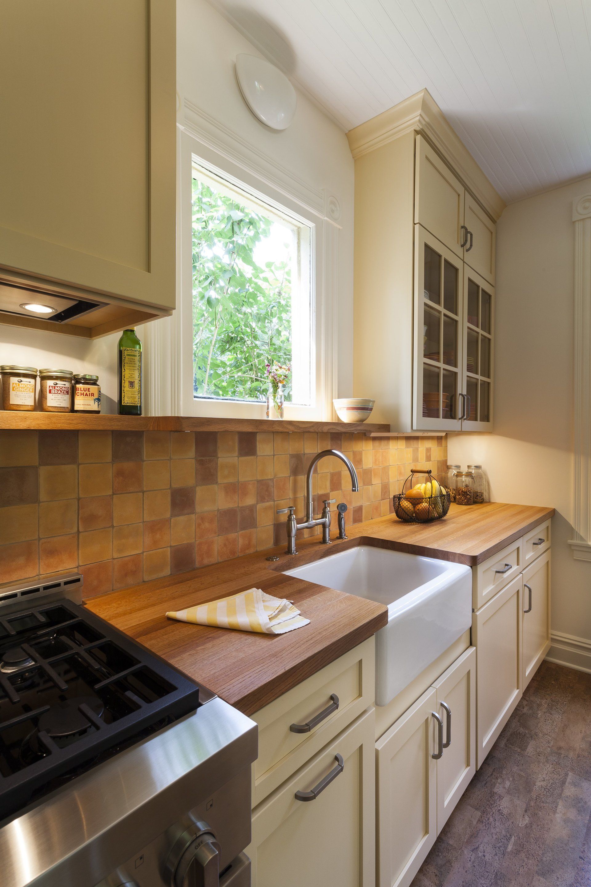 Bright kitchen with cream cabinets, wood counters, tiled backsplash, and a sink by a window.