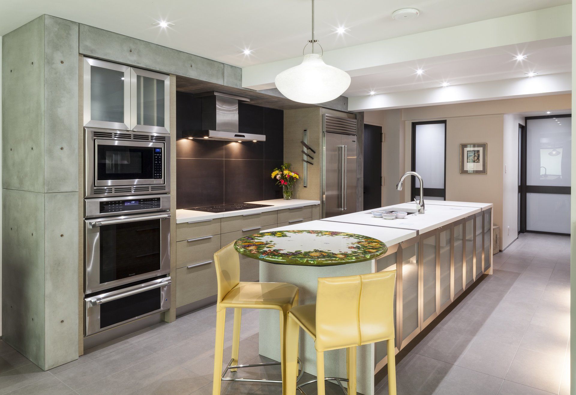 Modern kitchen with island, yellow stools, built-in ovens, and white pendant lights