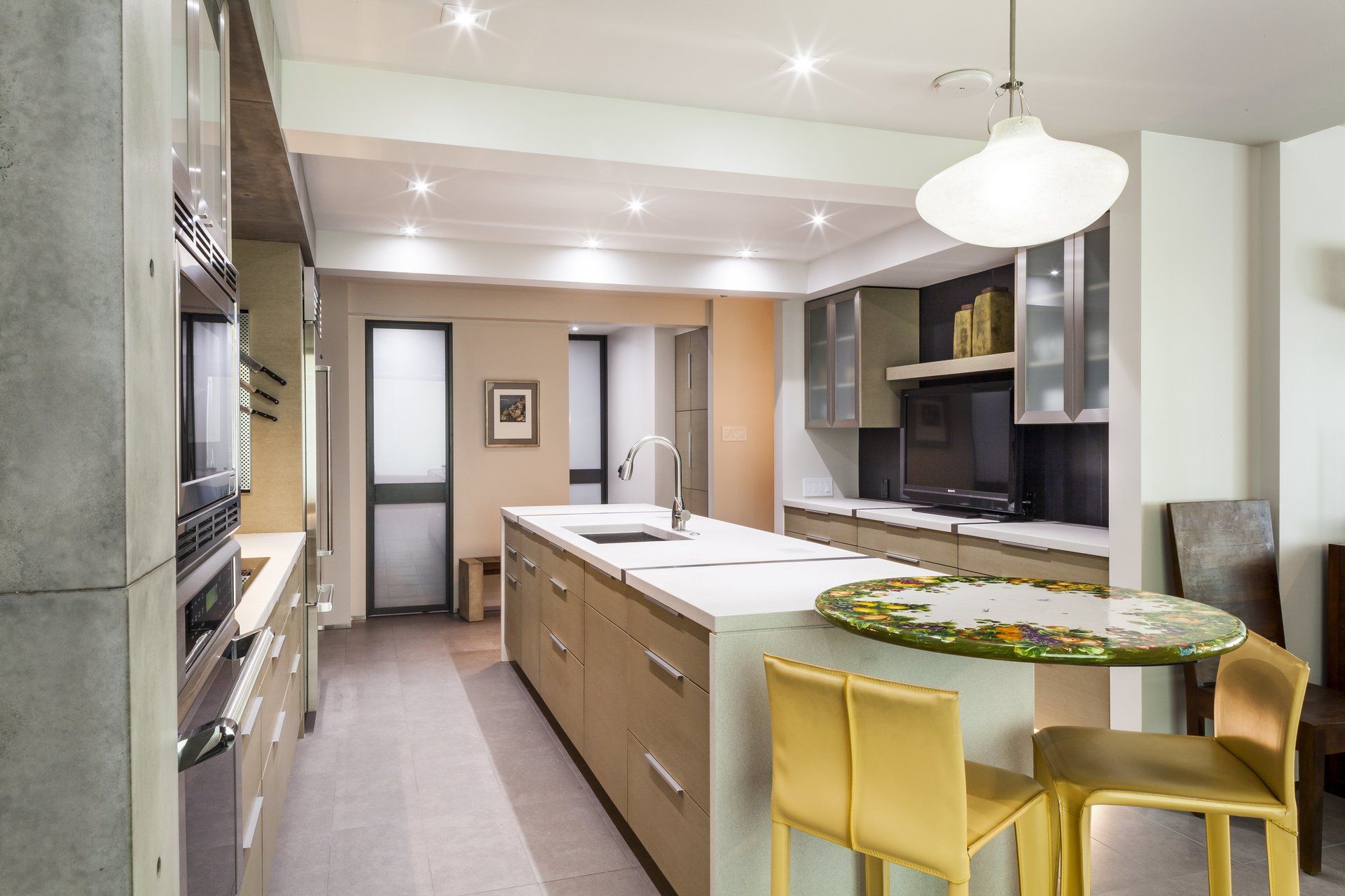 Modern kitchen with long island, yellow stools, white pendant lights, and gray cabinetry