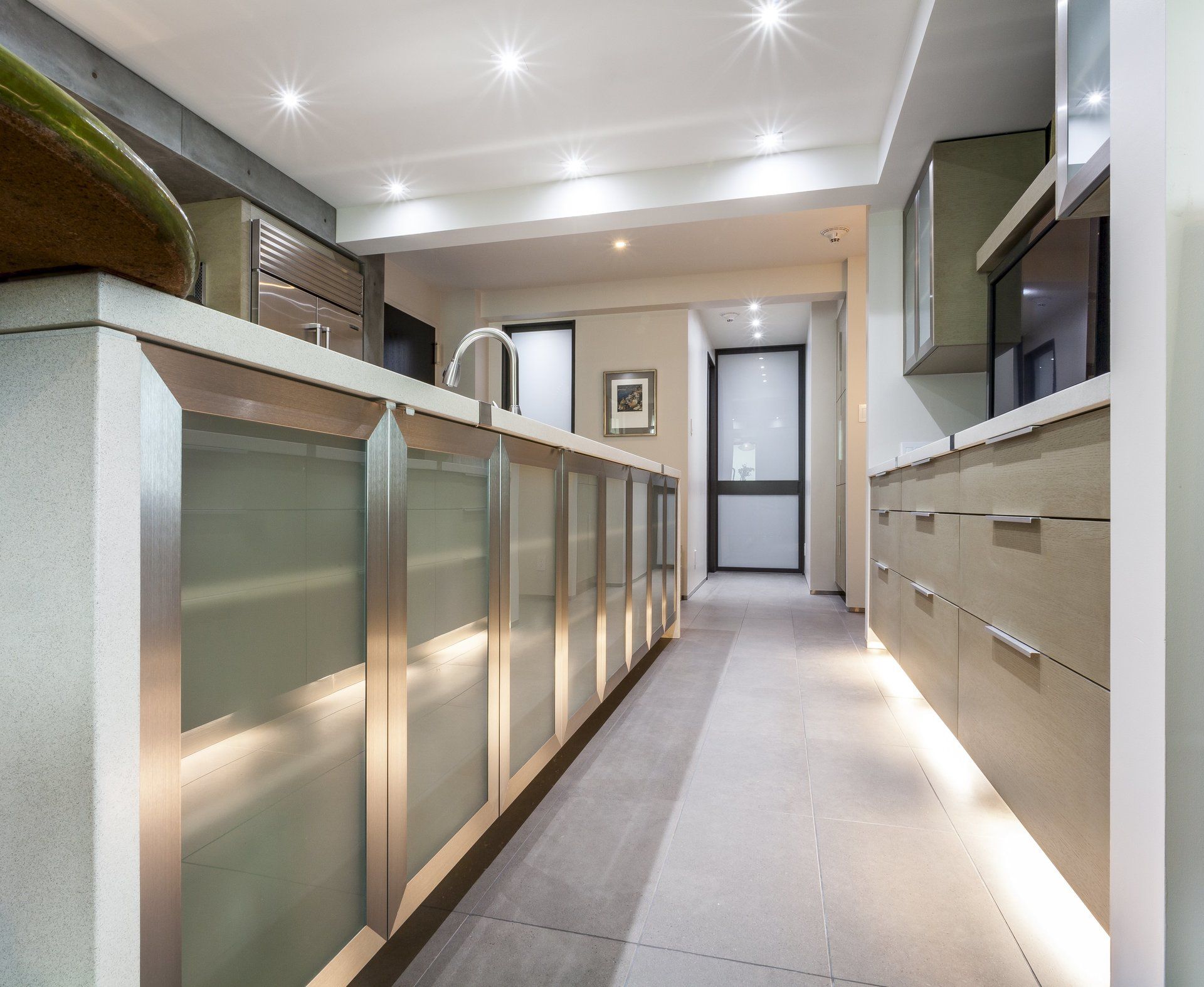 Modern kitchen hallway with light wood cabinets, frosted glass doors, and recessed ceiling lights.