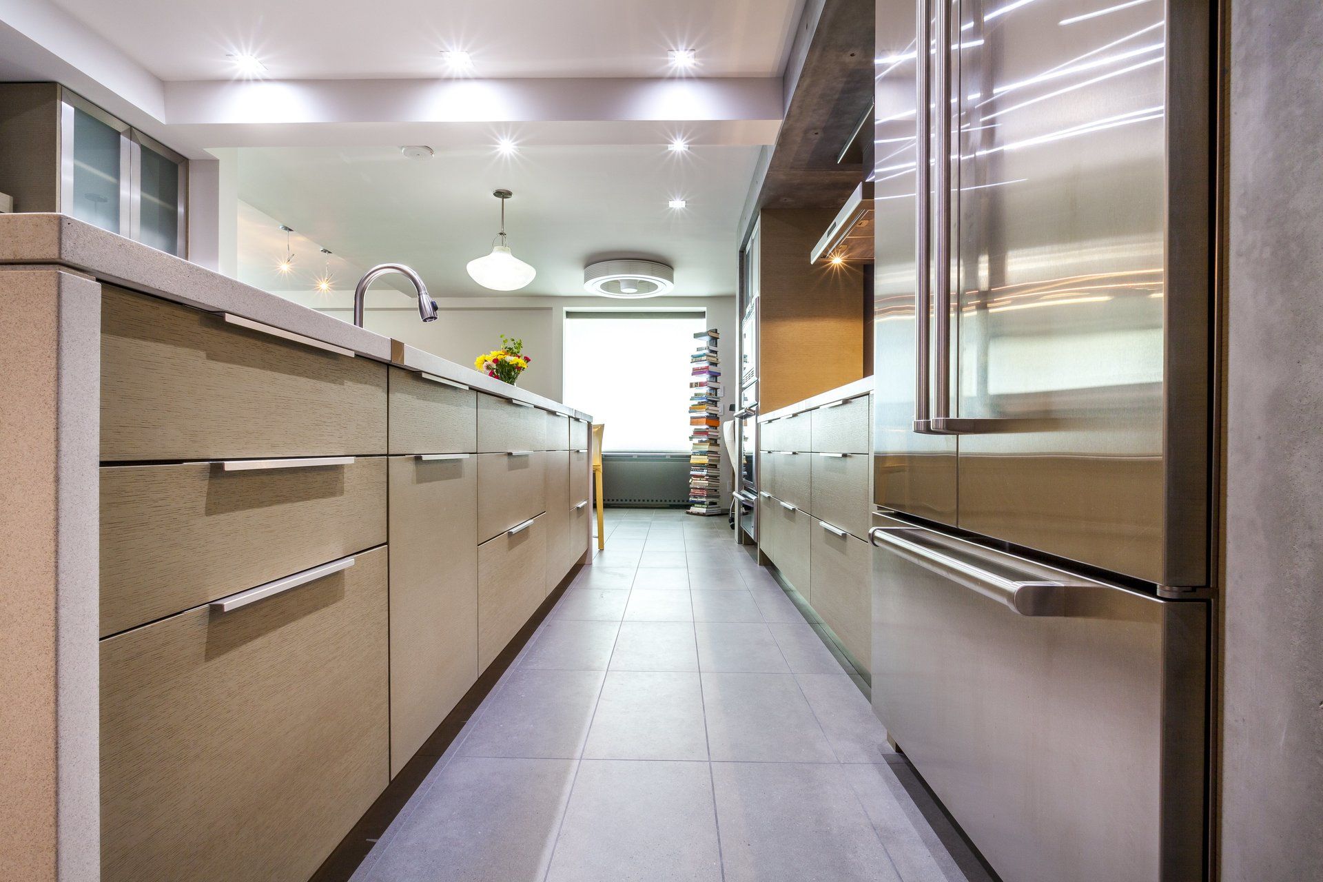 Modern kitchen with long stone counter, beige cabinets, and stainless steel appliances under recessed lights
