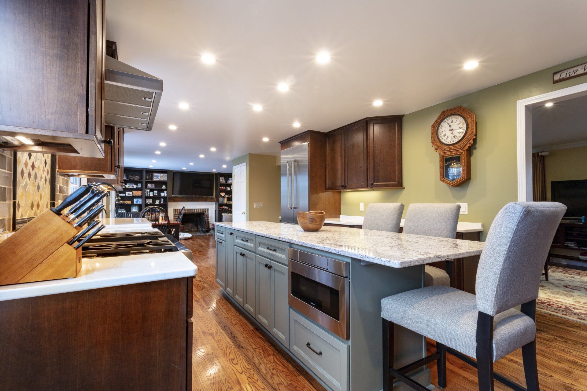 Modern kitchen with dark wood cabinets, granite island, bar stools, and bright recessed lighting