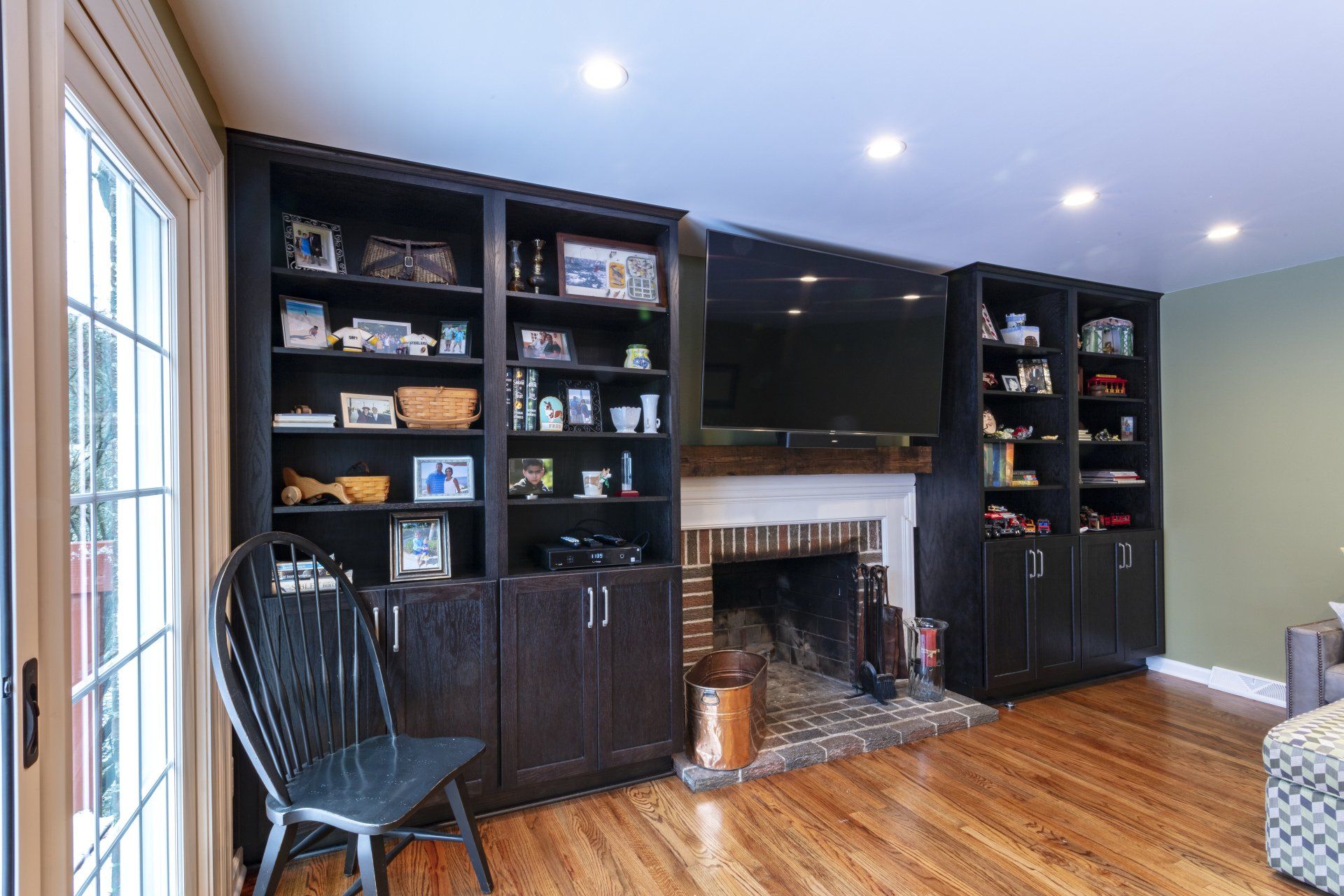 Living room with built-in black bookshelves, fireplace, wall-mounted TV, and hardwood floors