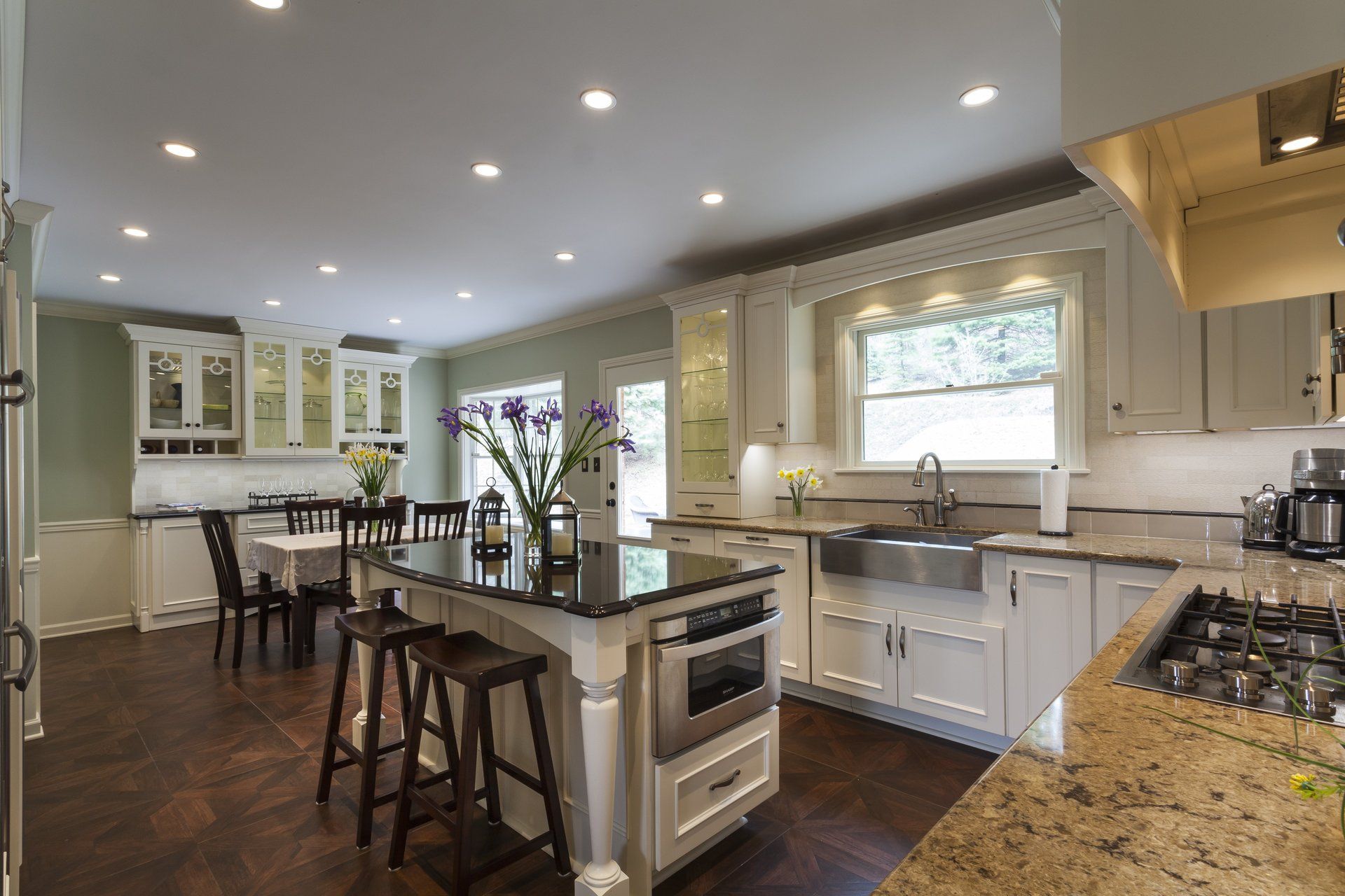 Bright modern kitchen with island, bar stools, white cabinets, granite counters, and recessed lighting.