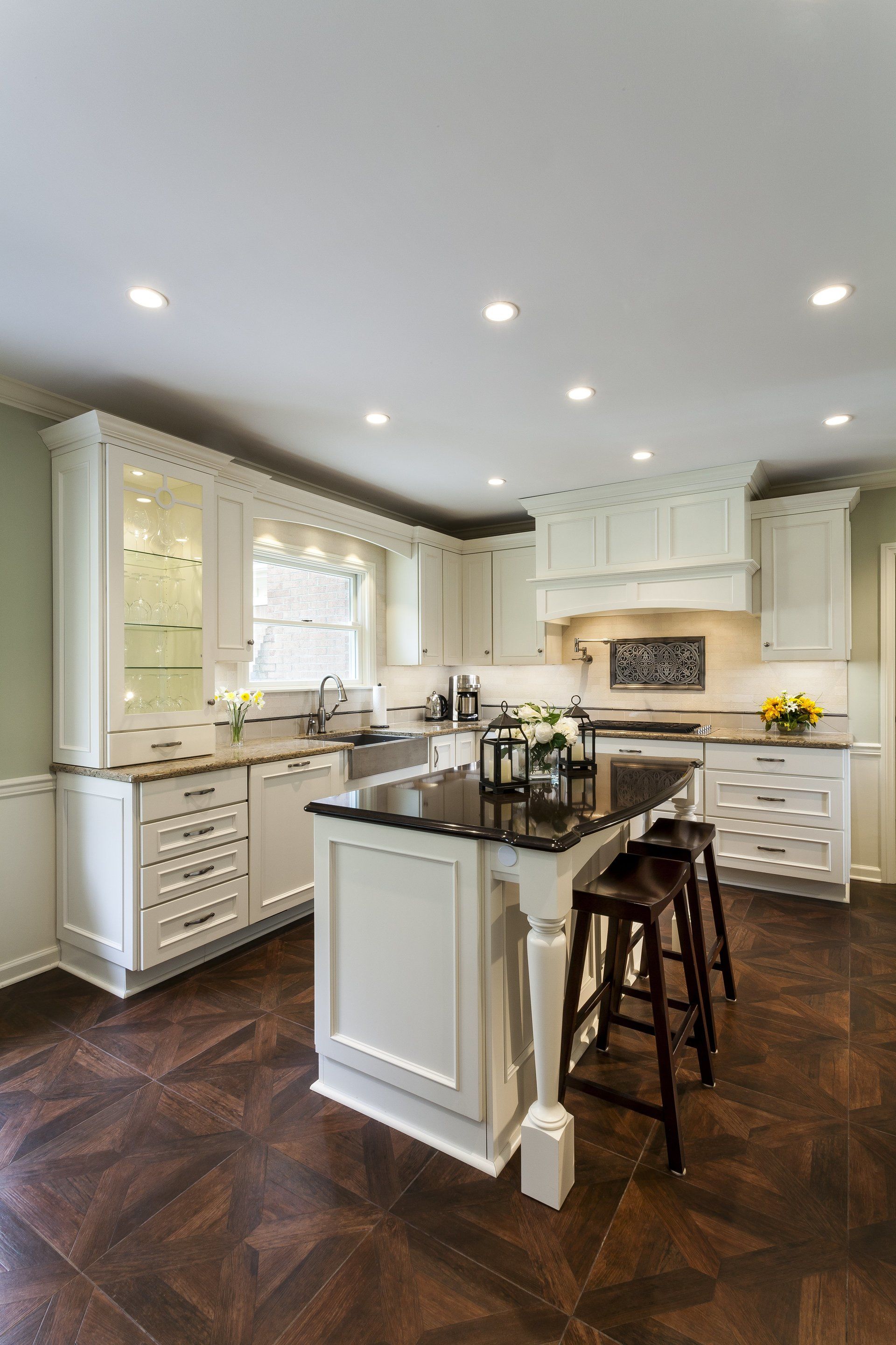 Bright white kitchen with island, dark wood floor, recessed lights, and barstools