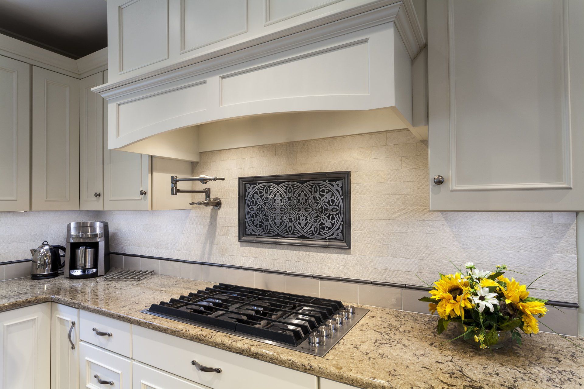 Modern kitchen with white cabinets, granite countertop, gas cooktop, and a small yellow flower arrangement.