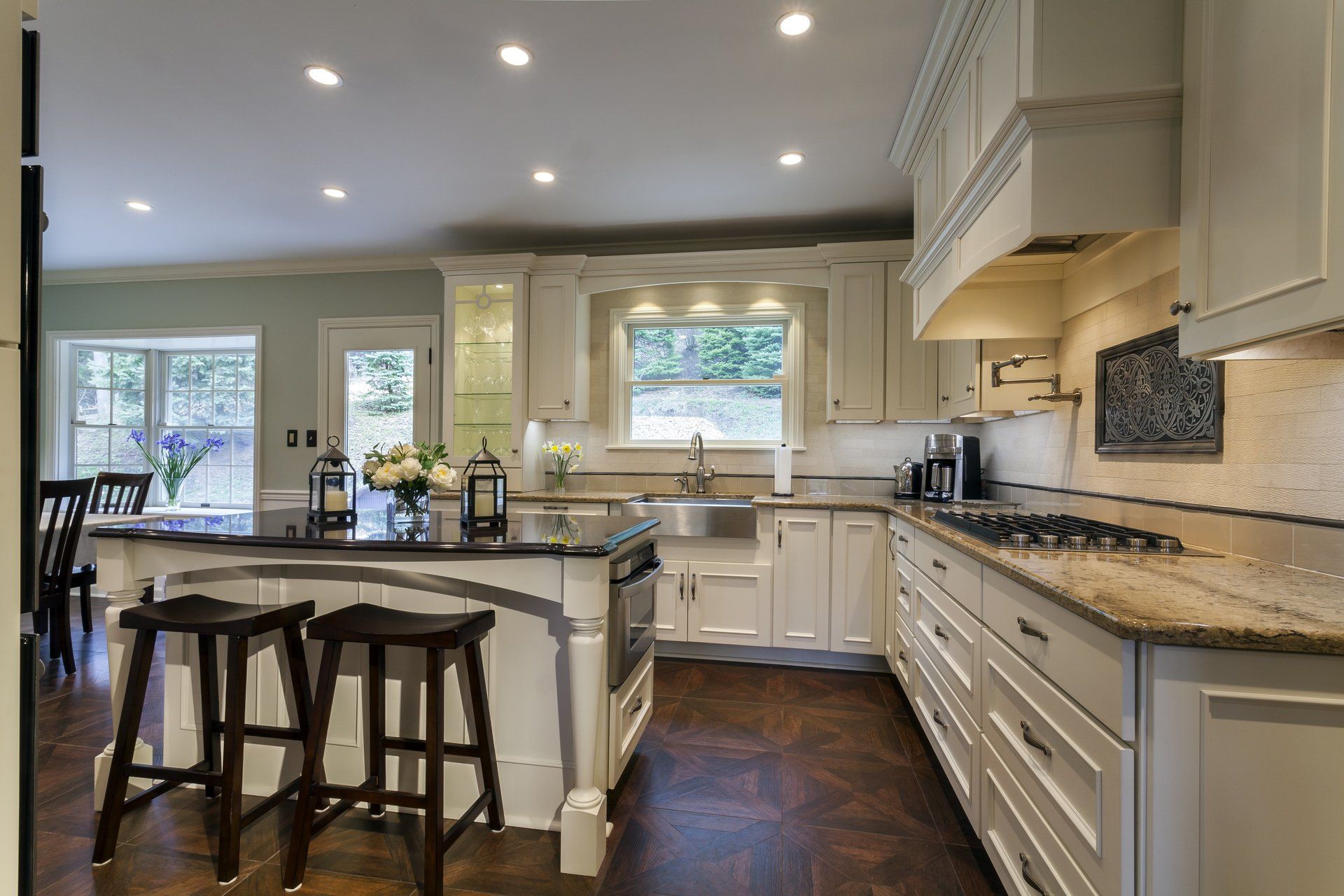 Bright, modern kitchen with white cabinets, dark island, granite counters, and bar stools by a window.