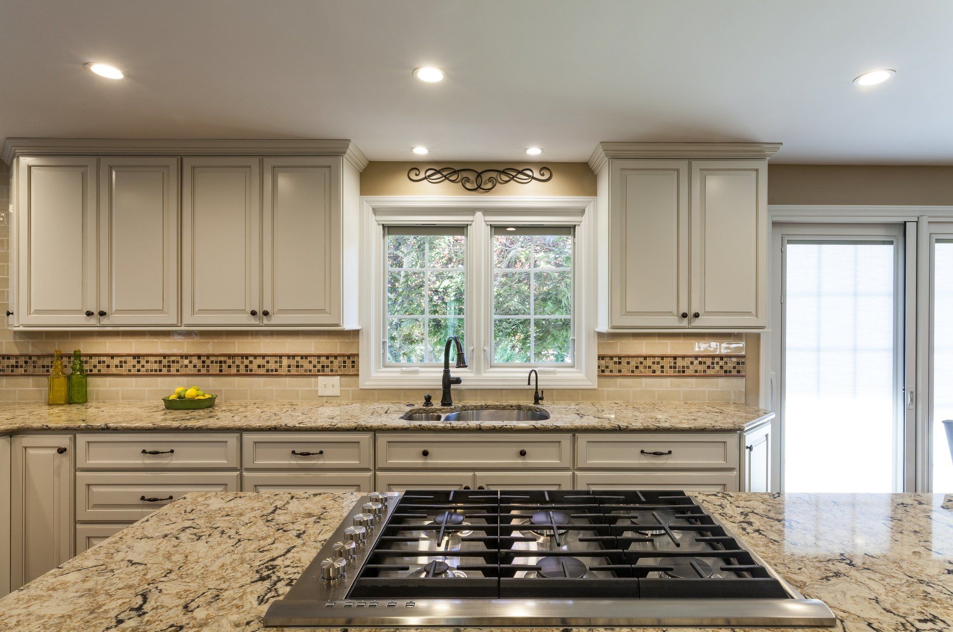 Bright kitchen with granite island, beige cabinets, recessed lights, and a window above the sink.