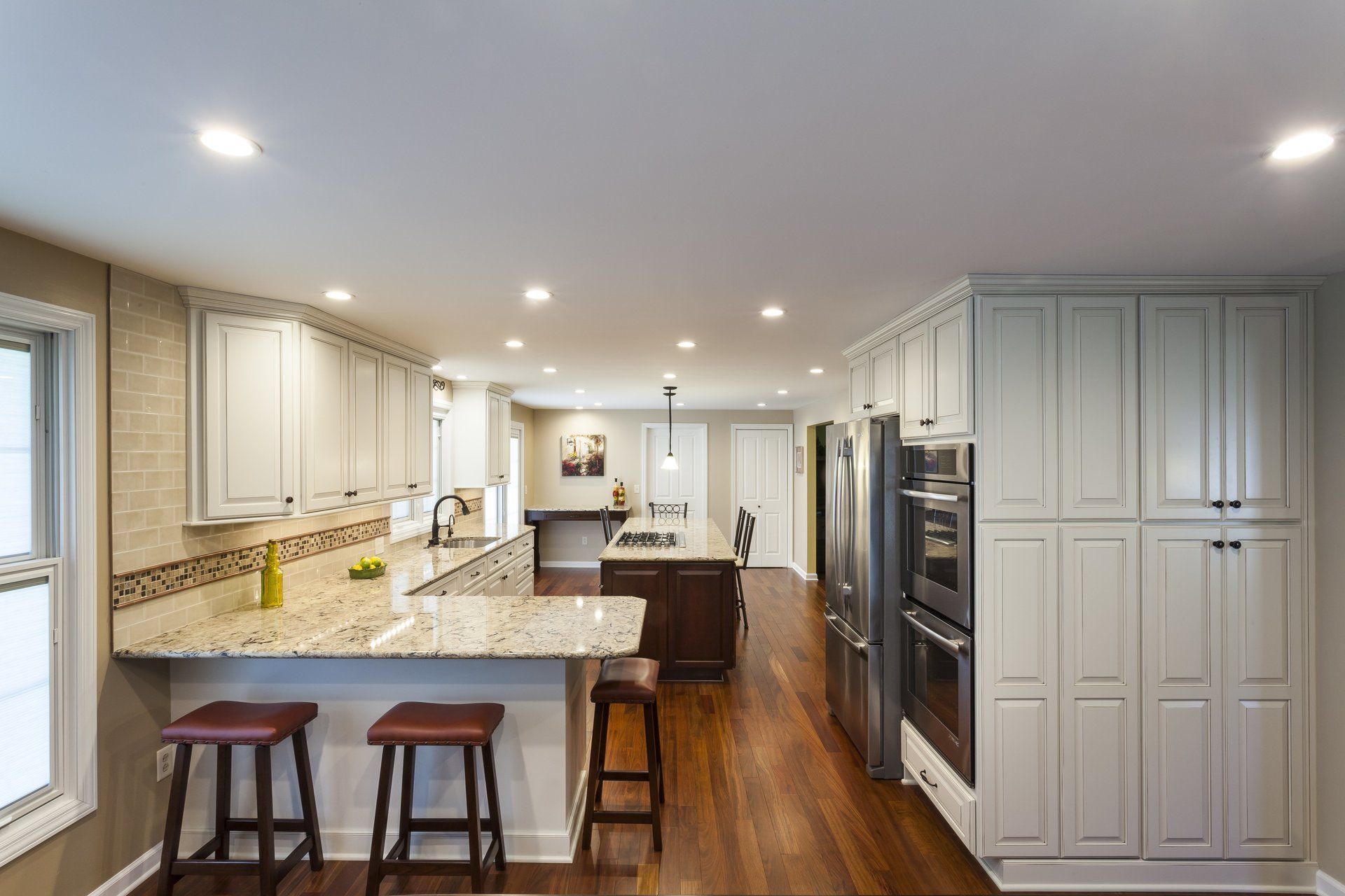 Bright white kitchen with island, bar stools, wood floors, and stainless steel appliances.