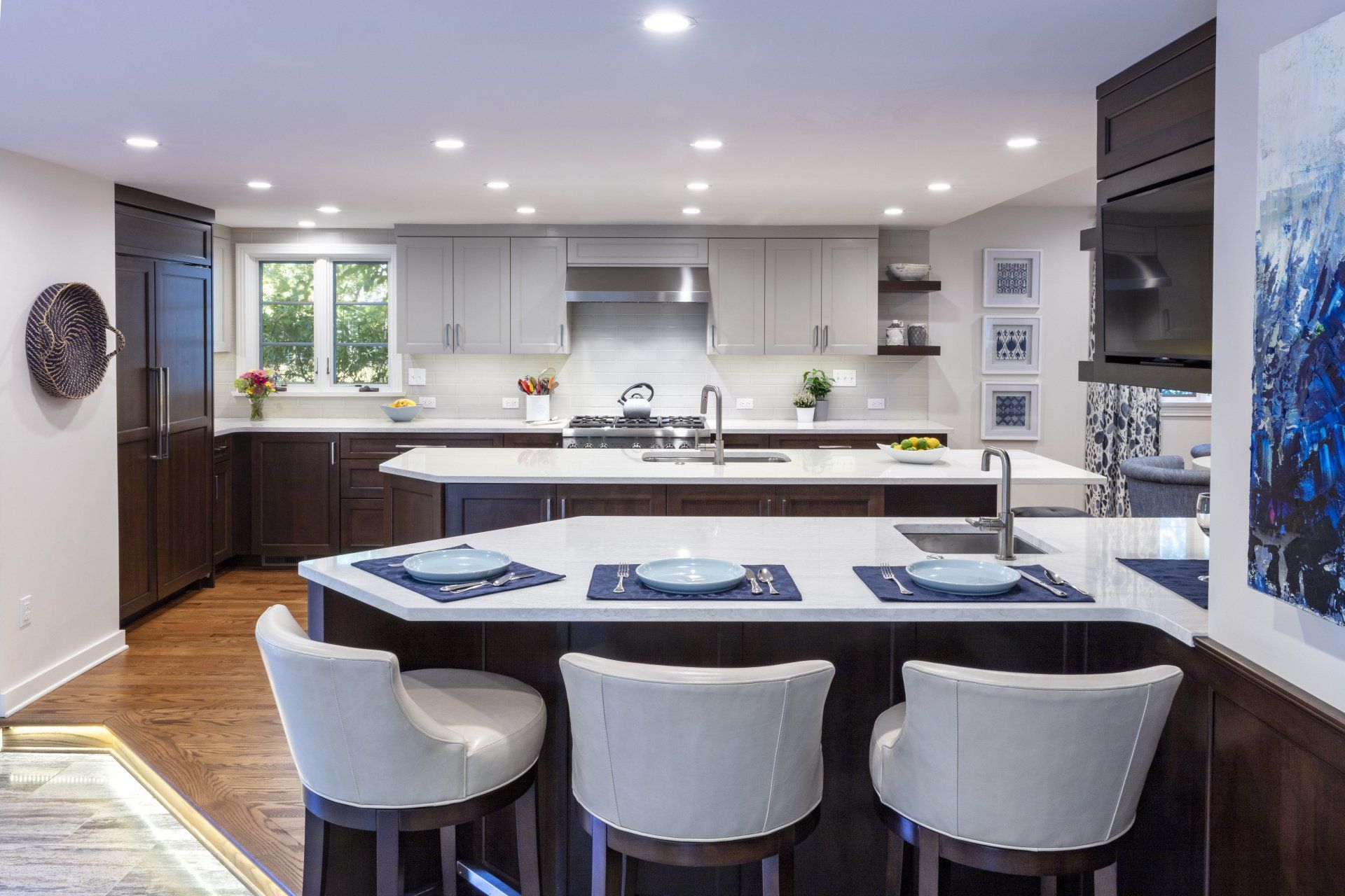 Modern open kitchen with white island, dark barstools, stainless appliances, and recessed lighting