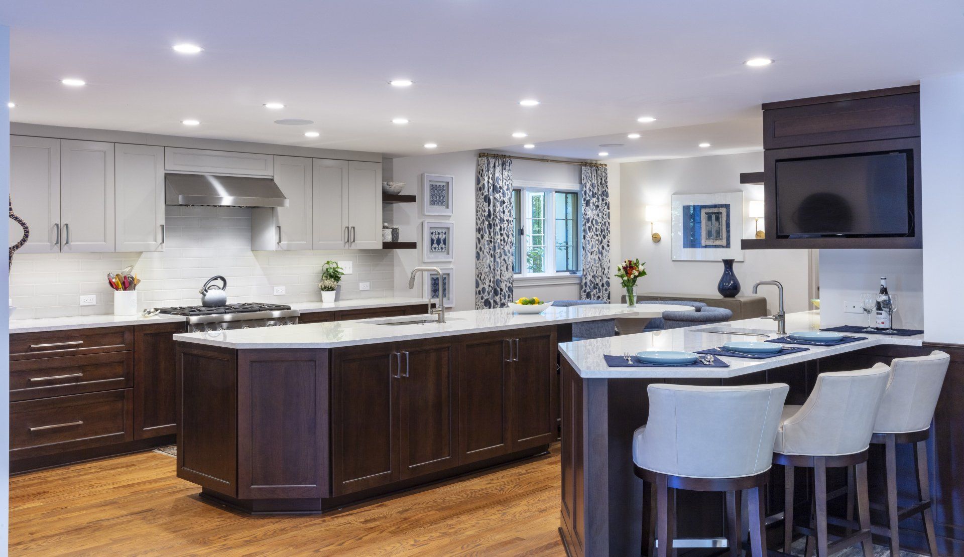 Modern open-plan kitchen with dark wood island, white countertops, bar stools, and stainless appliances