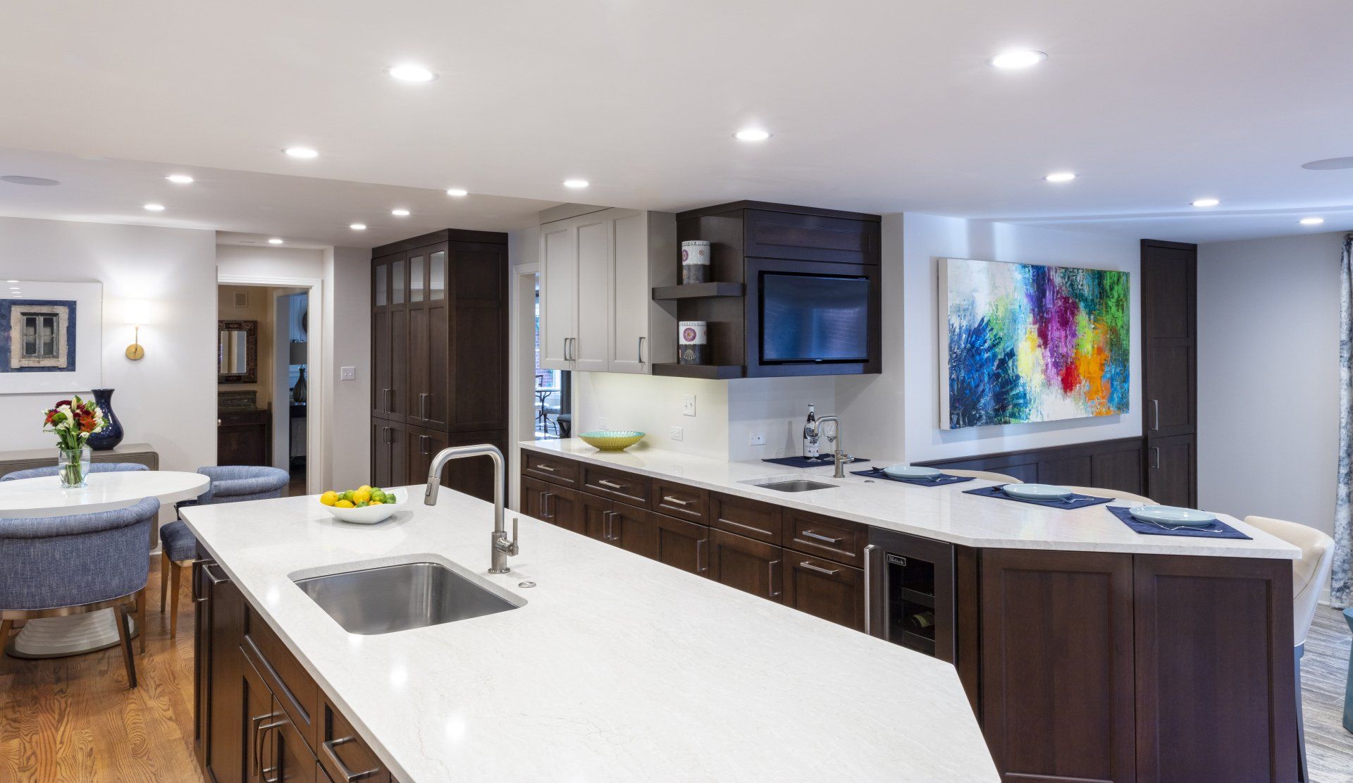 Modern kitchen with large white island, dark cabinets, recessed lighting, and colorful wall art