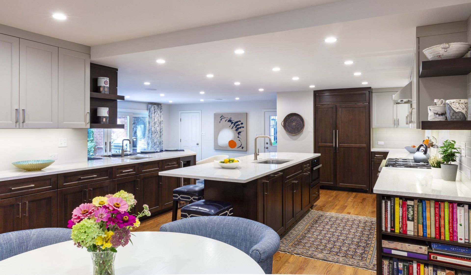 Modern kitchen with dark wood island, white cabinets, colorful flowers, and a bookshelf in the foreground