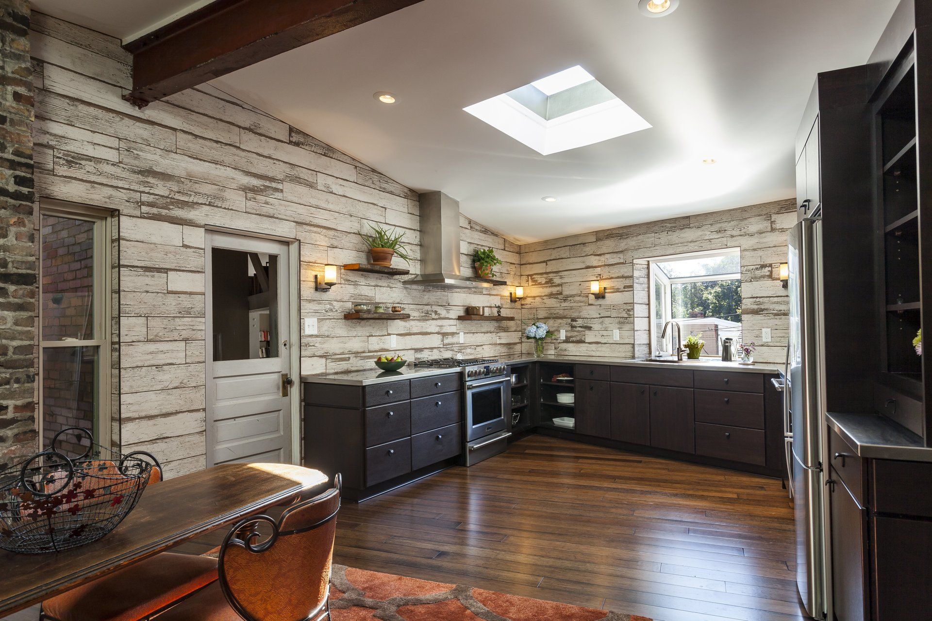 Bright modern kitchen with white brick walls, dark cabinets, hardwood floors, and skylight.