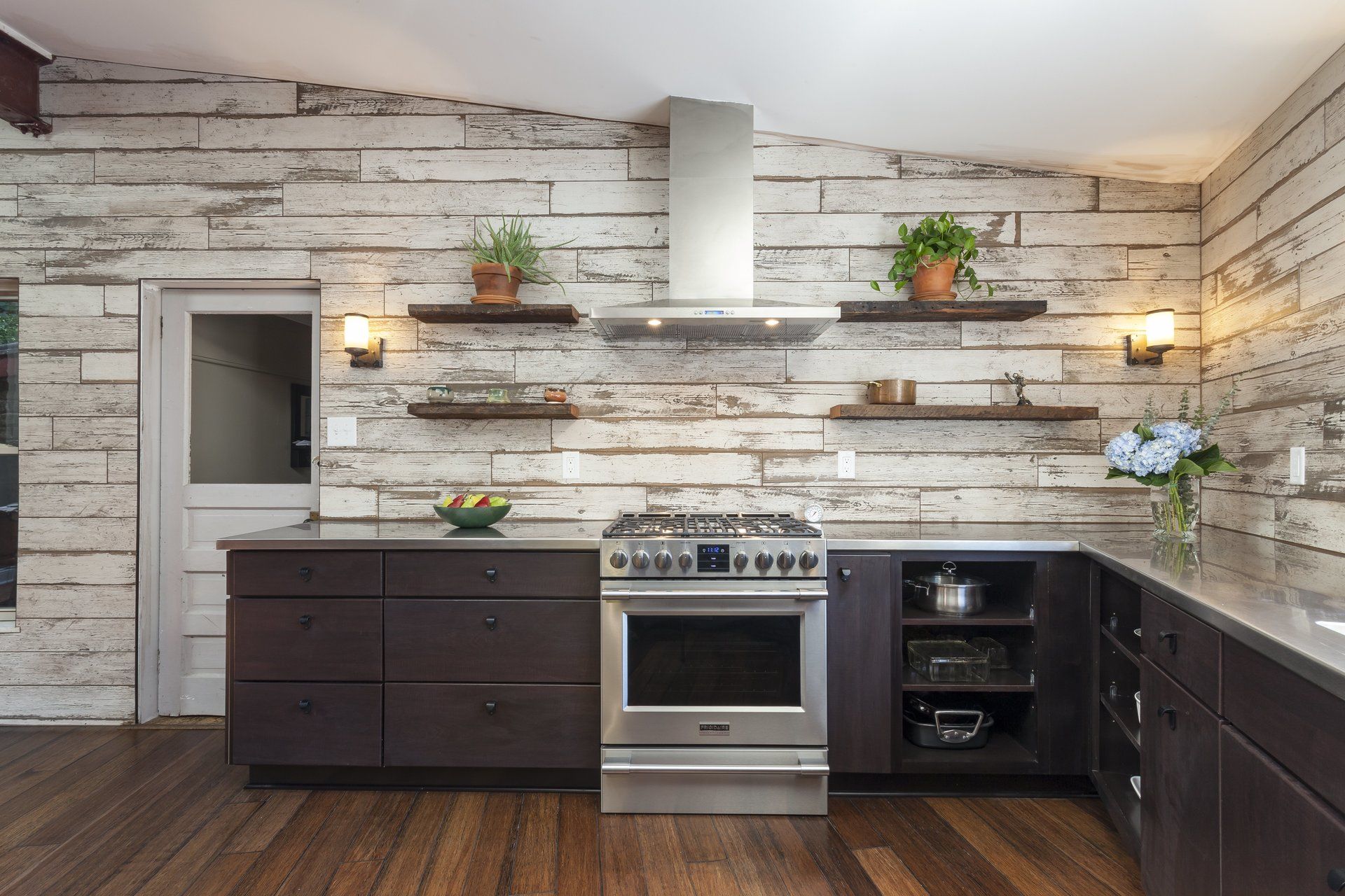 Modern kitchen with dark cabinets, wood floors, open shelves, and stainless steel appliances