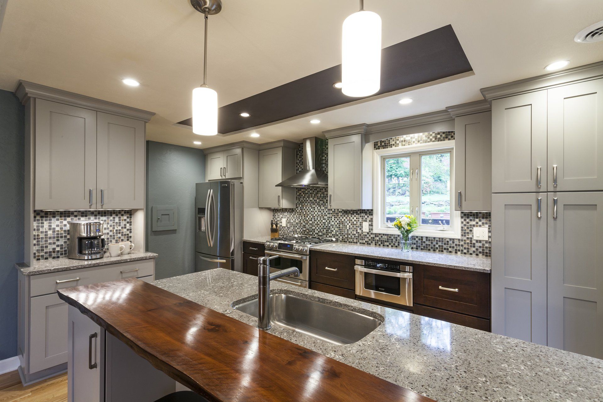 Modern kitchen with gray cabinets, granite island, pendant lights, and a window over the sink