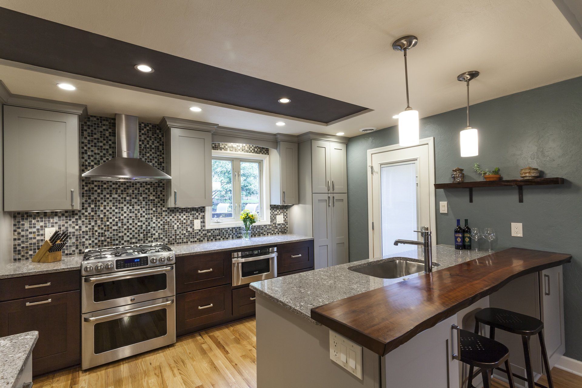 Modern kitchen with dark cabinets, stainless appliances, mosaic backsplash, and a granite island under pendant lights