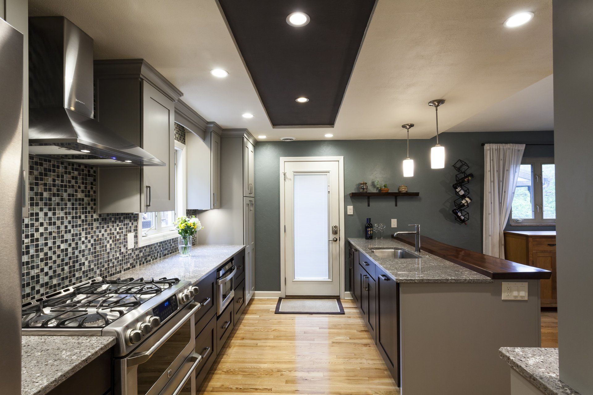 Modern kitchen with gray cabinets, granite island, mosaic backsplash, and wood floors