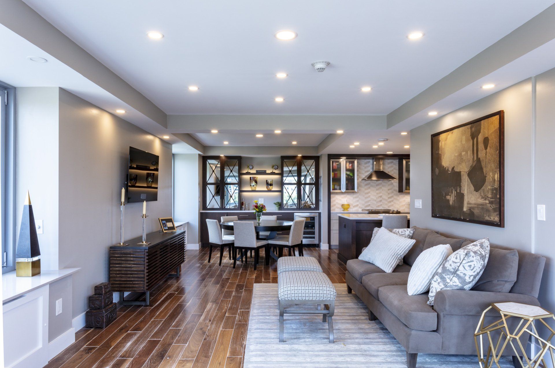 Modern open-plan living room with gray sofa, dining area, dark wood floors, and built-in shelves