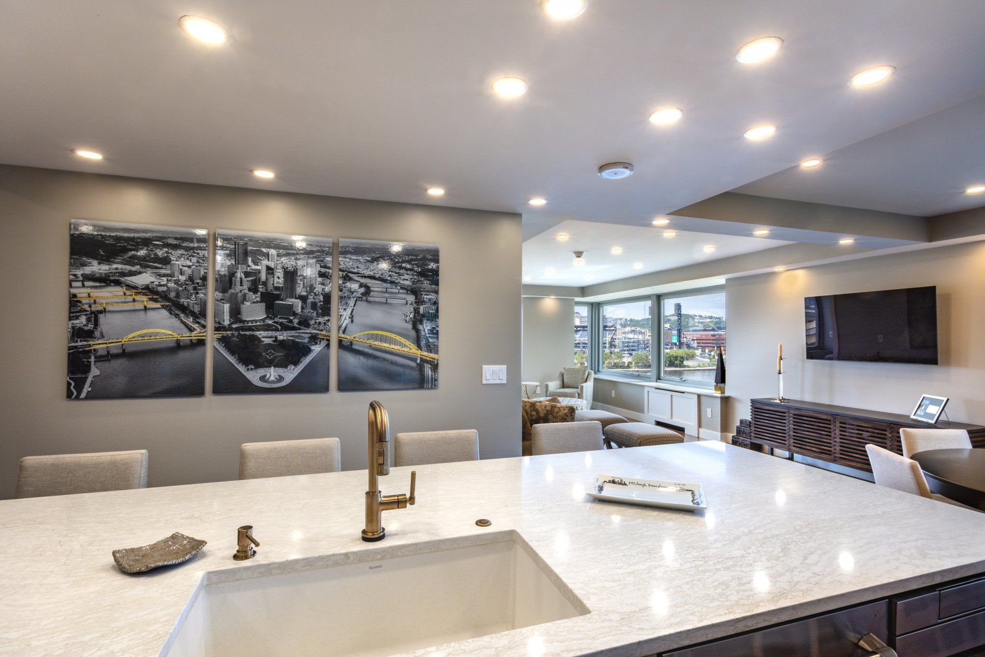 Modern open kitchen with white island, gold faucet, recessed lights, and wall art overlooking a living area