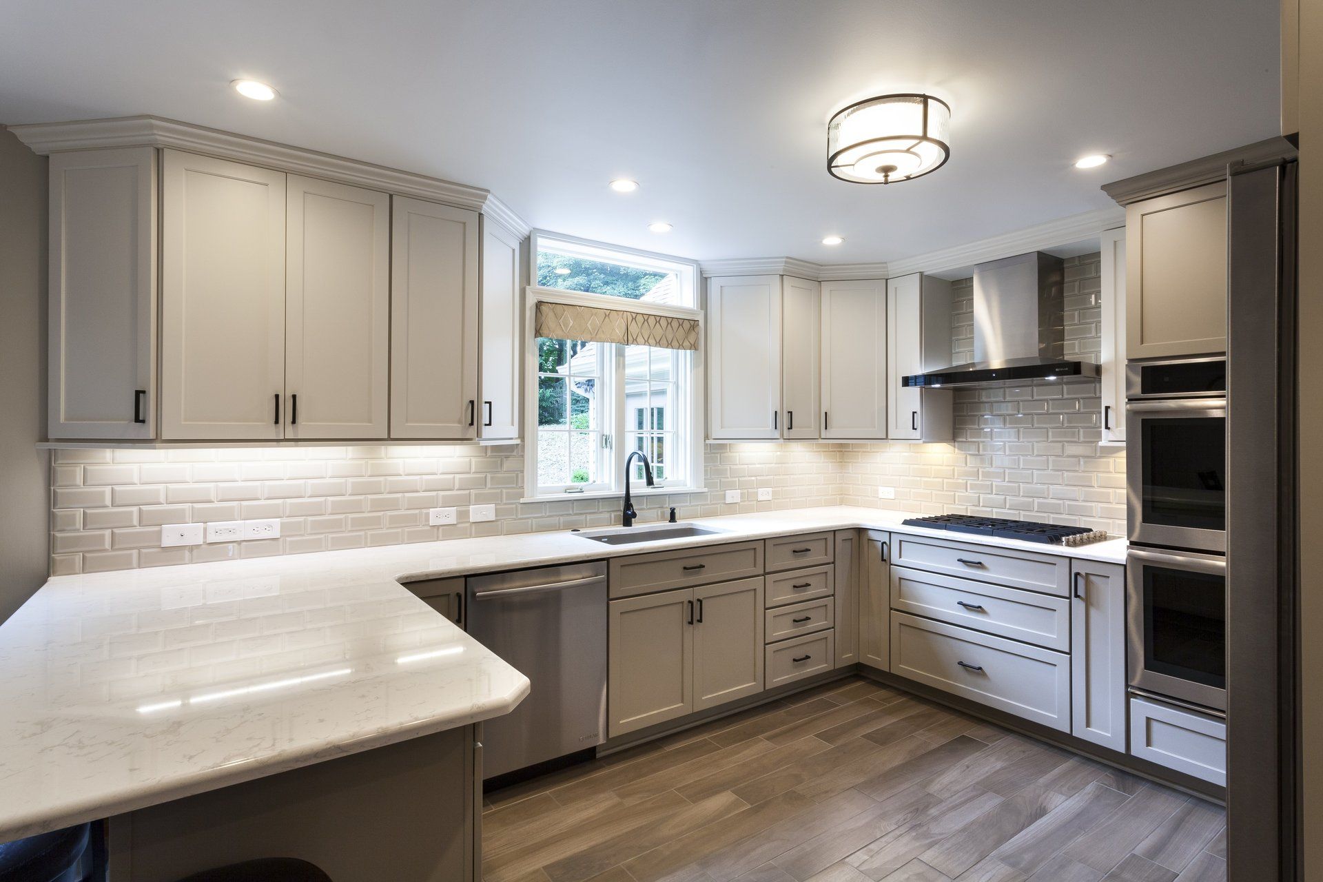 Modern white kitchen with gray cabinets, stainless appliances, island, and window over sink