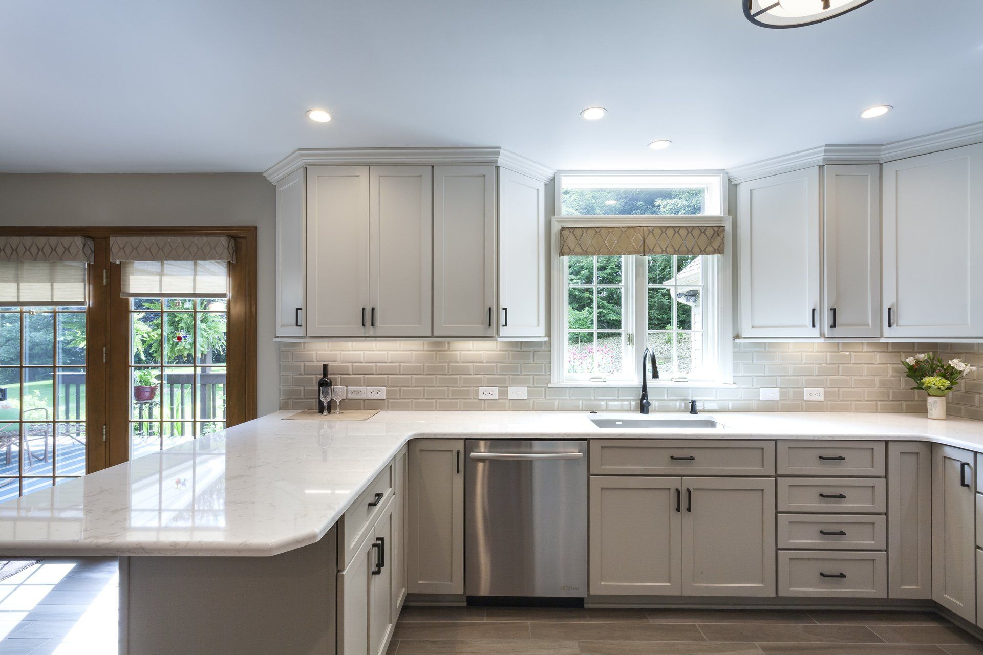 Bright modern kitchen with white cabinets, marble island, stainless dishwasher, and glass doors to a backyard.