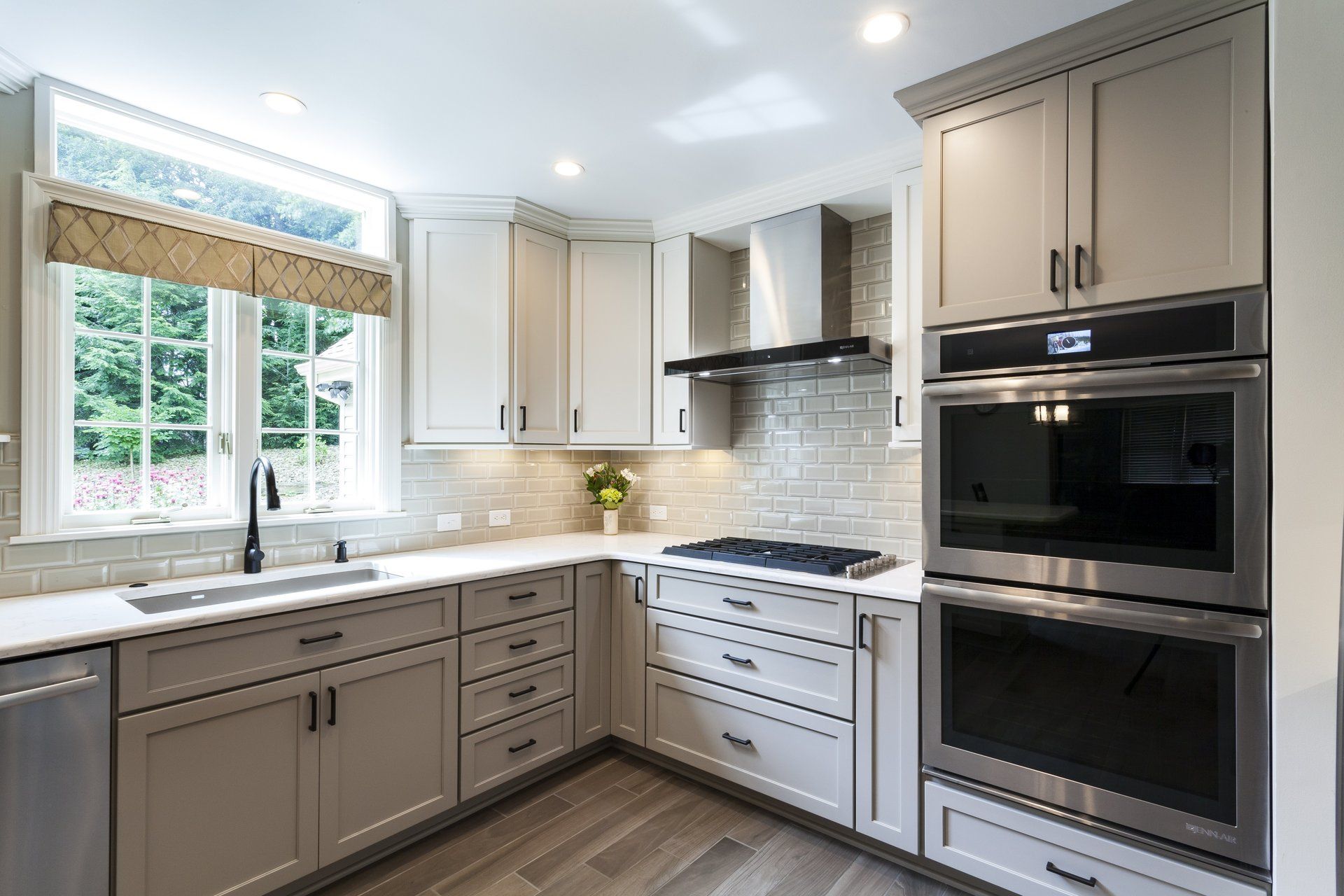 Bright modern kitchen with white cabinets, beige accents, stainless appliances, and a large window over the sink