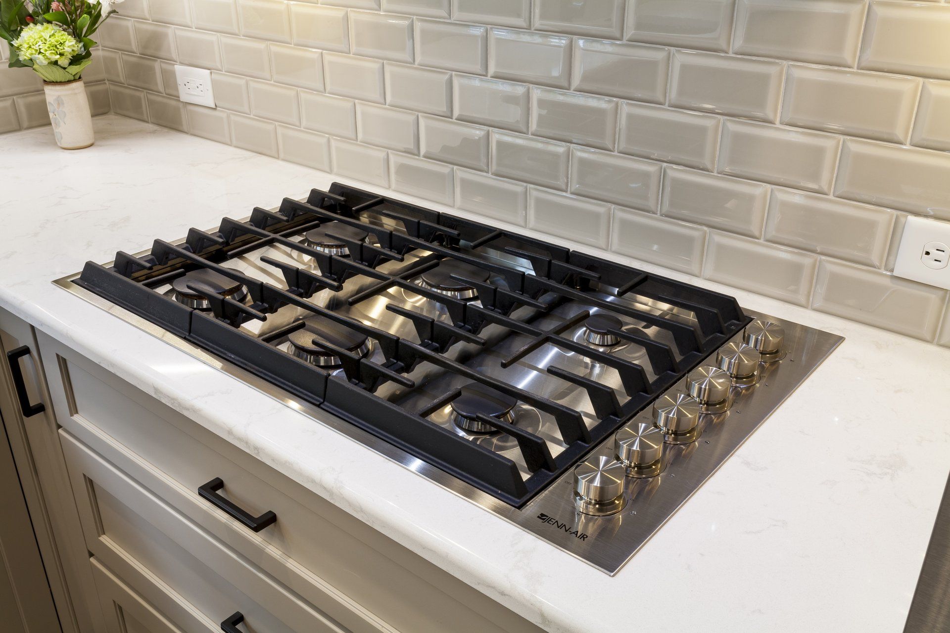 Stainless steel gas cooktop on a white kitchen countertop with tiled backsplash