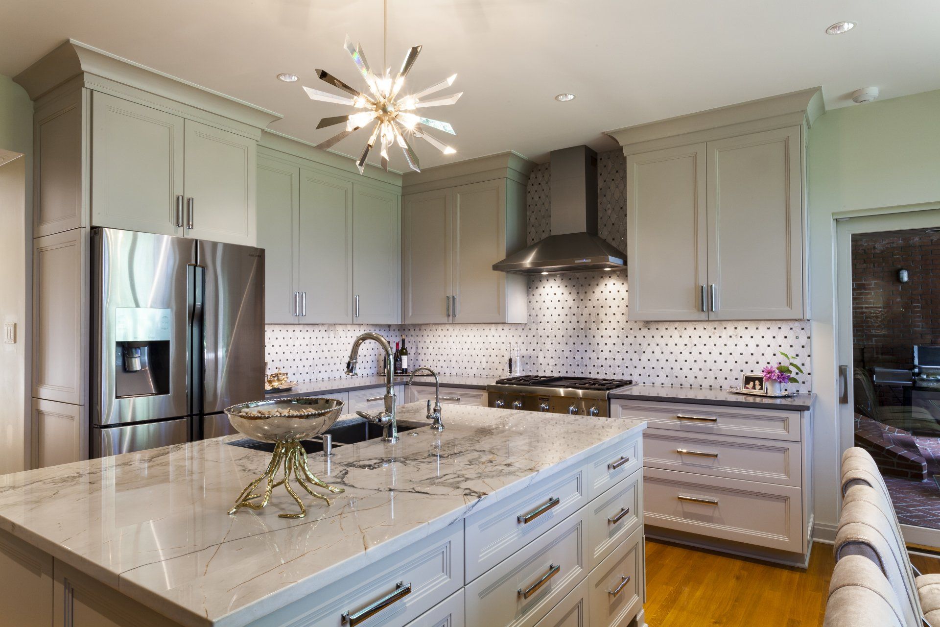 Bright modern kitchen with gray cabinets, white marble island, stainless fridge, and chandelier