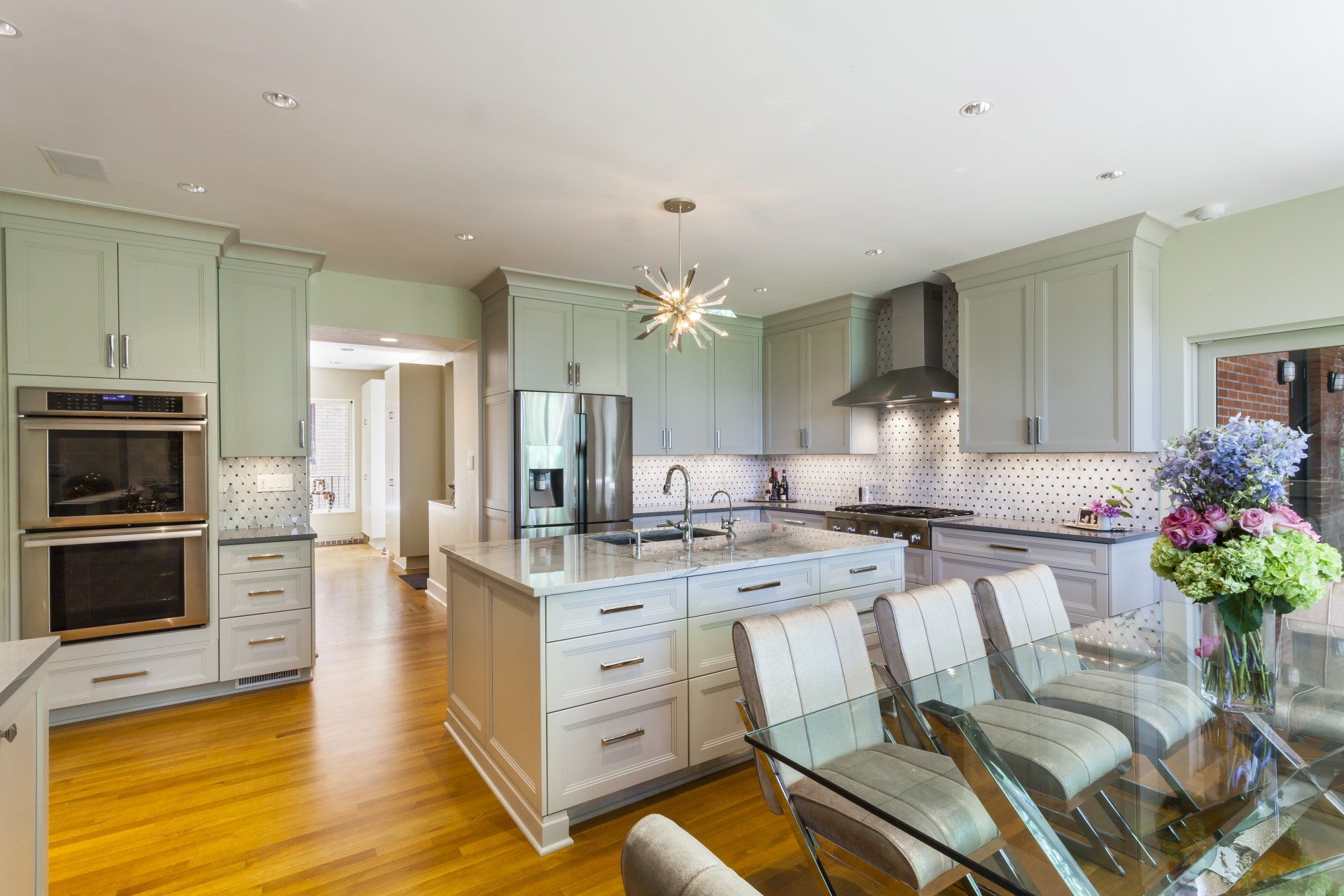 Bright kitchen with pale green cabinets, stainless steel appliances, island, and glass dining table