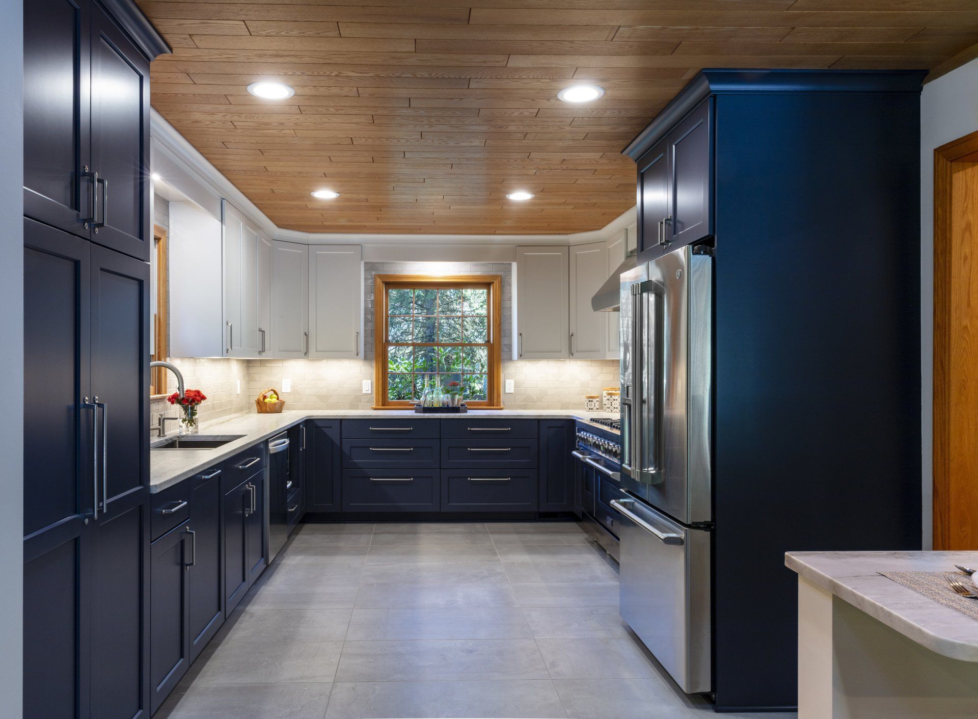 Modern kitchen with dark blue cabinets, wood ceiling, stainless appliances, and a central window