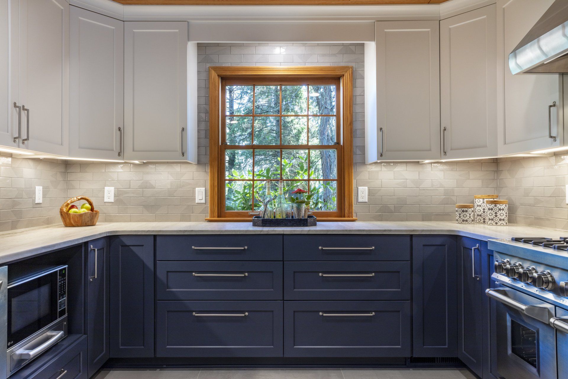 Modern kitchen with navy lower cabinets, white uppers, stainless appliances, and a window above the sink.