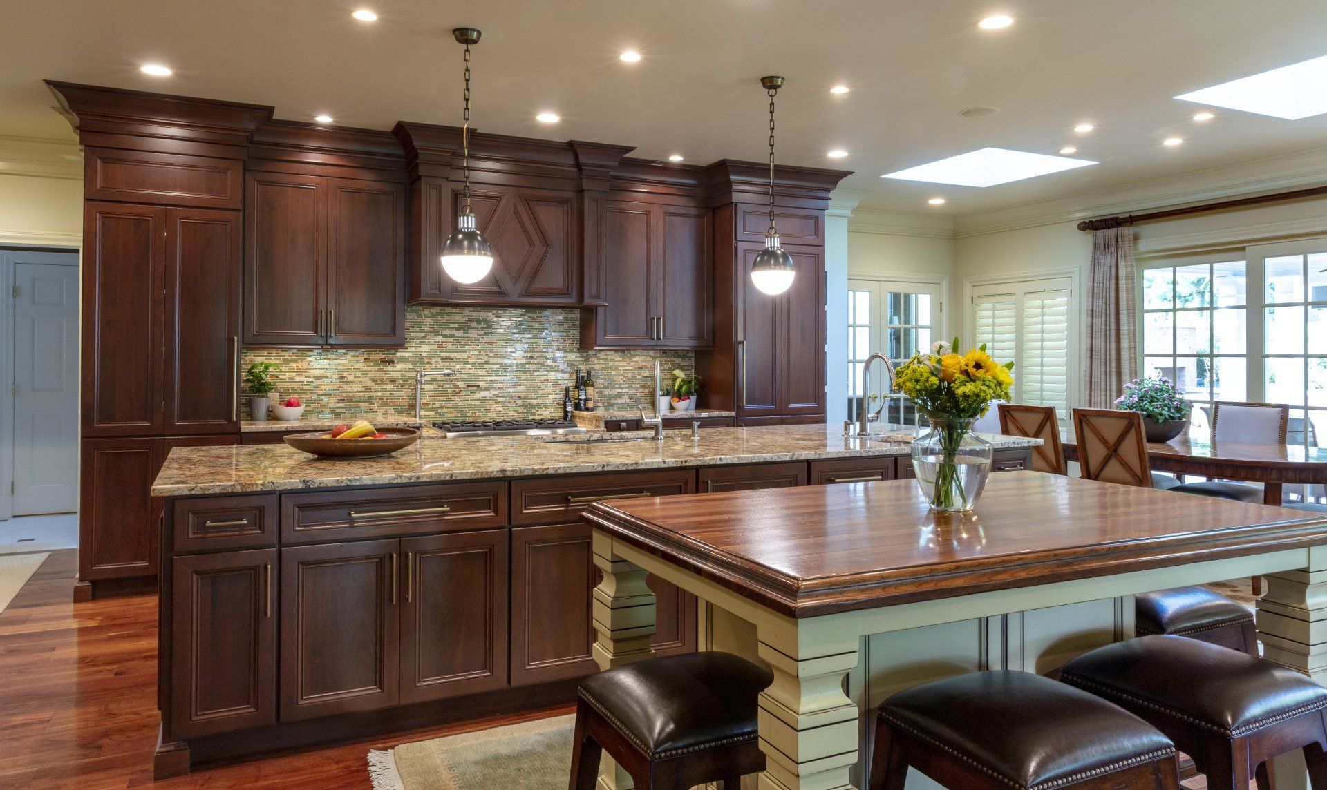 Elegant kitchen with dark wood cabinets, granite island, pendant lights, and a breakfast nook by windows.