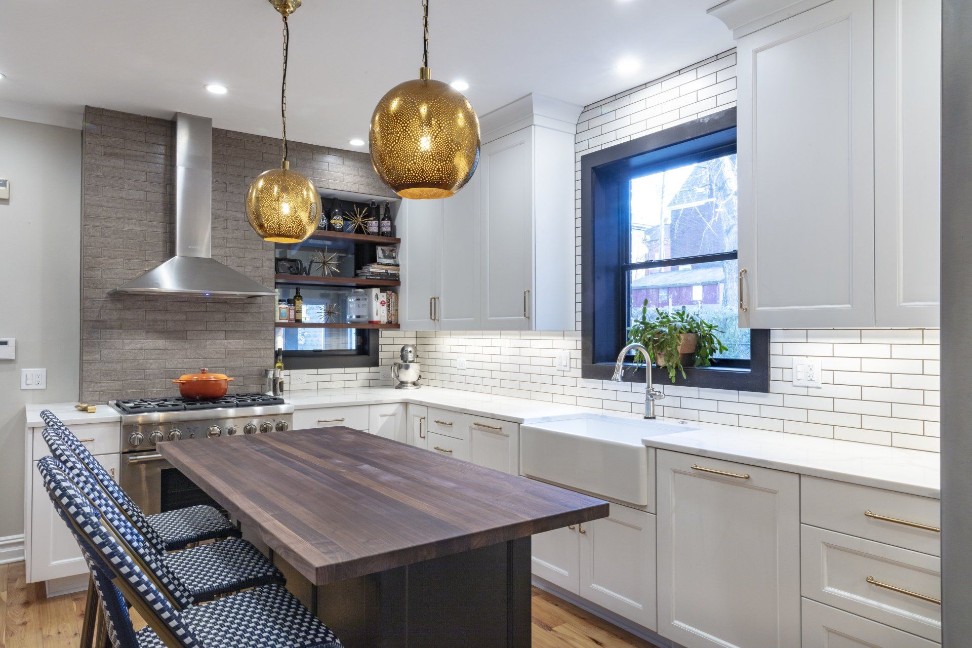Modern kitchen with white cabinets, dark island table, brass pendant lights, and a large window