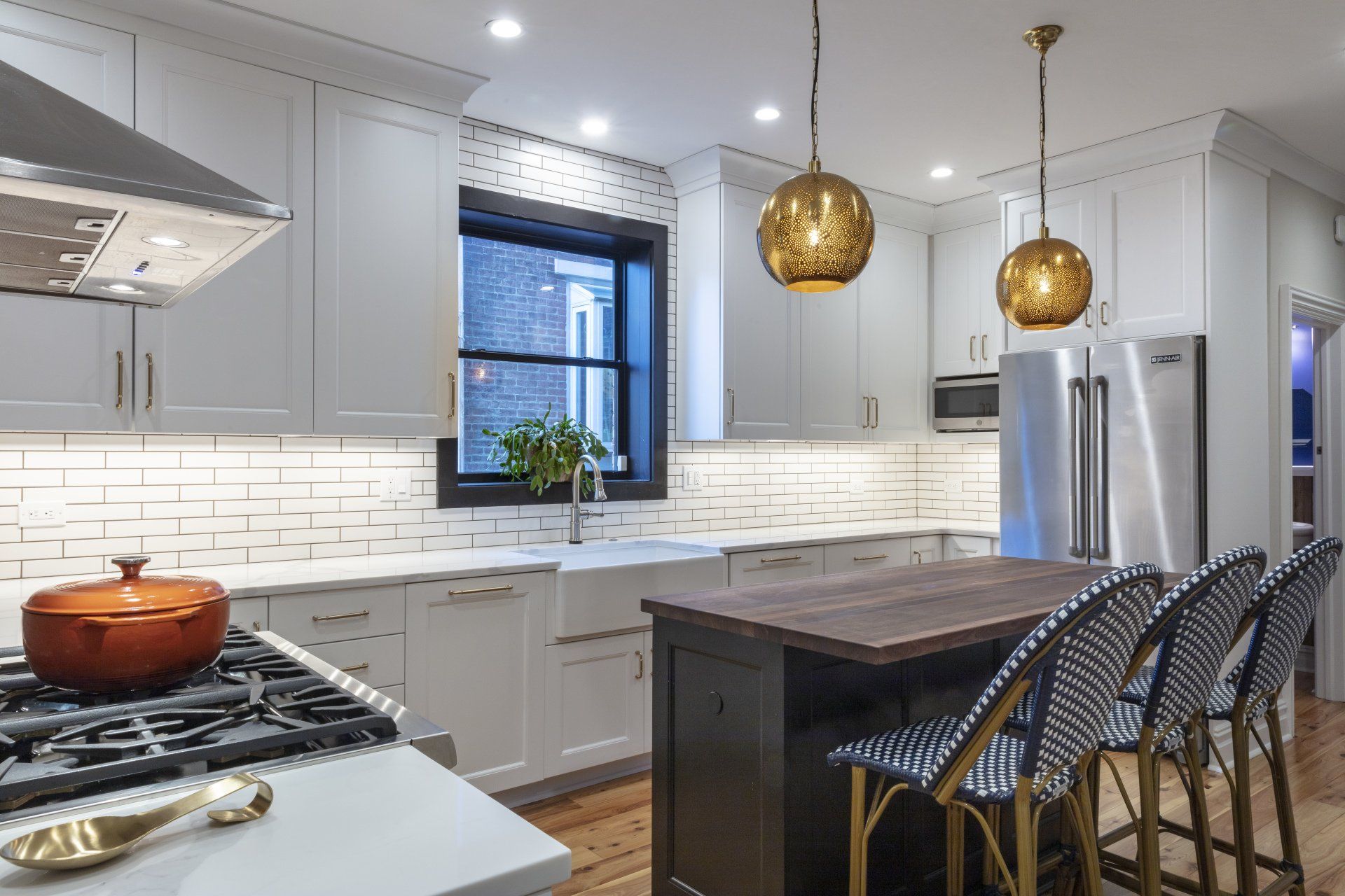 Modern white kitchen with island, brass pendant lights, stainless fridge, and dark wood stools